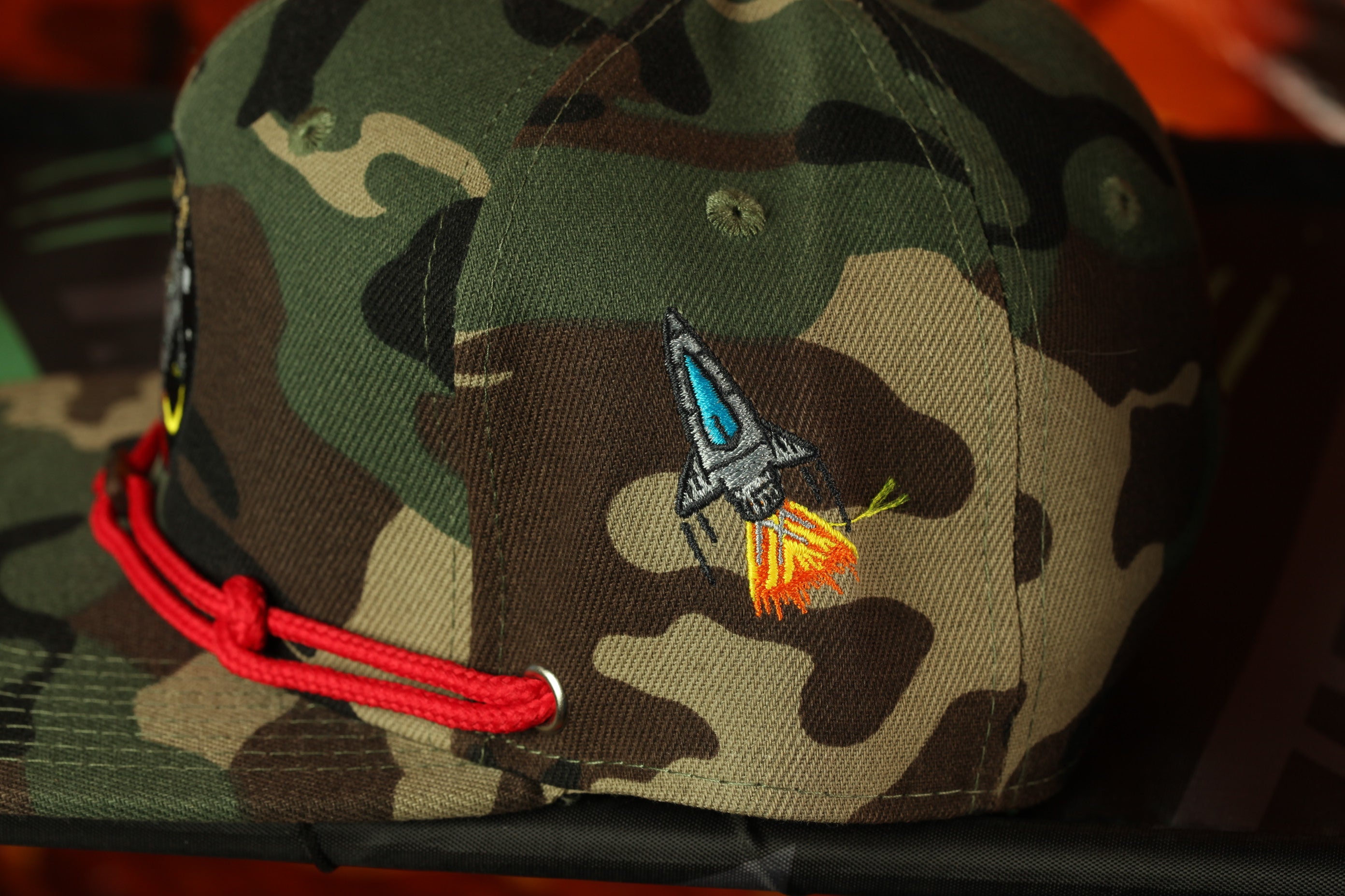 A camouflage baseball cap with a rocket ship embroidered on it.