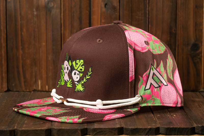 A brown baseball cap with a floral pattern and a white string around the brim, placed on a wooden surface.