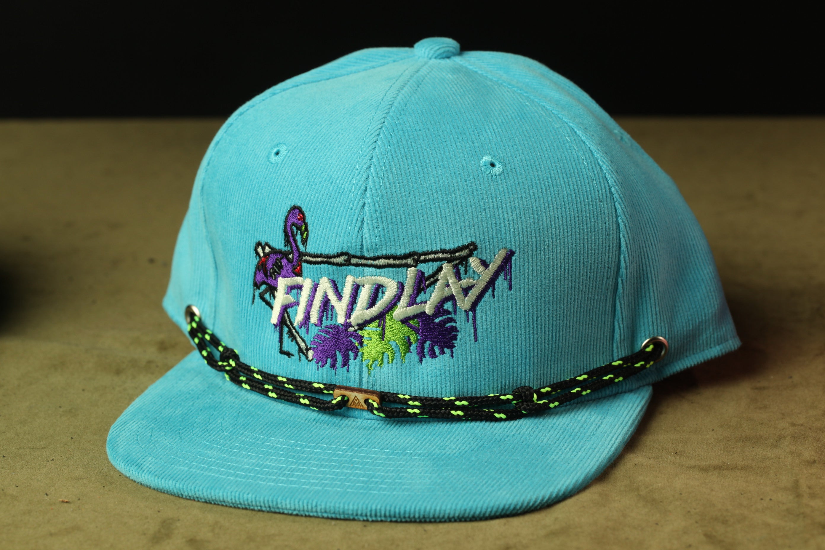 A turquoise baseball cap with a graphic design and the word "FINDLAY" printed on it.