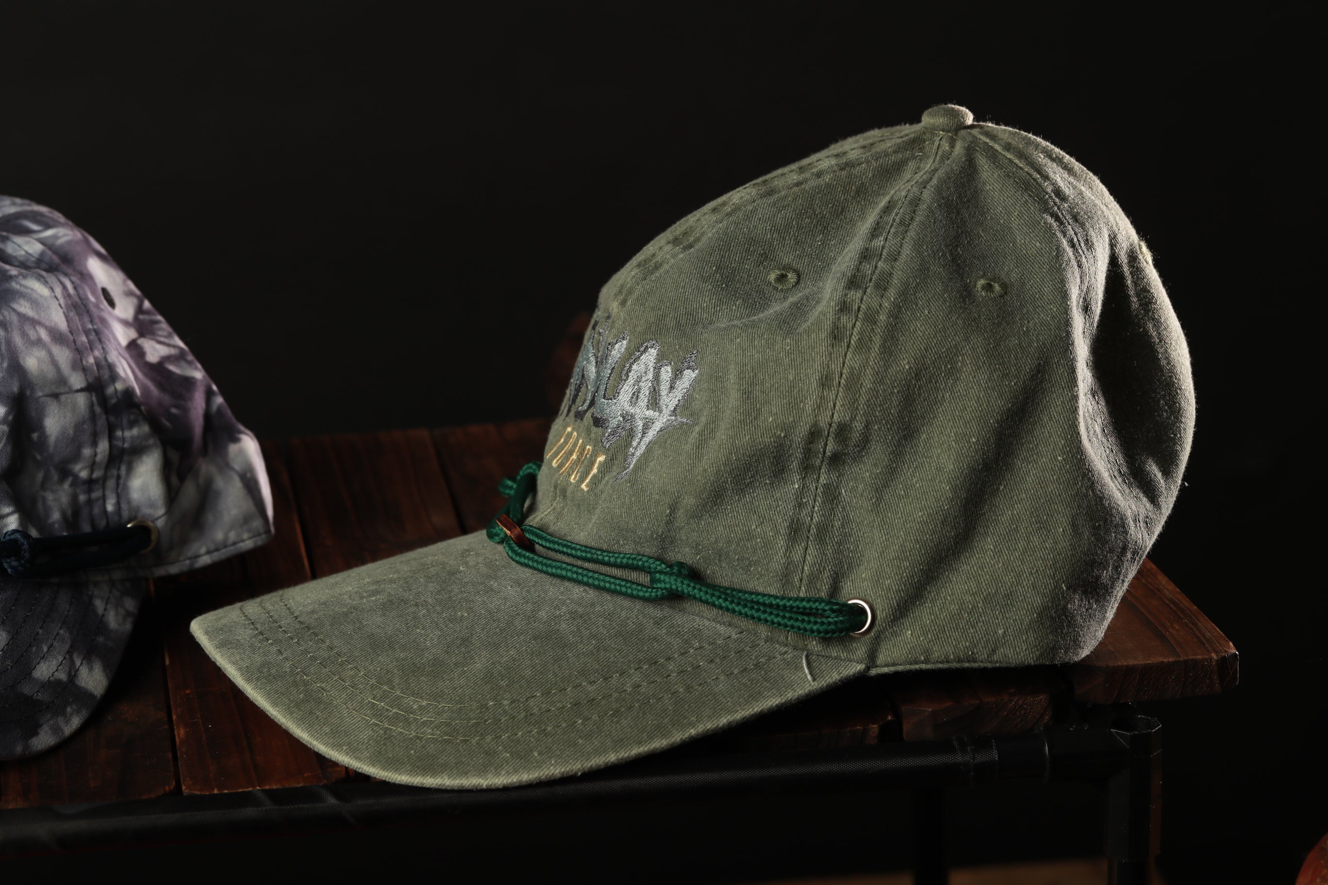 A green baseball cap with a green string around the brim is placed on a wooden surface.