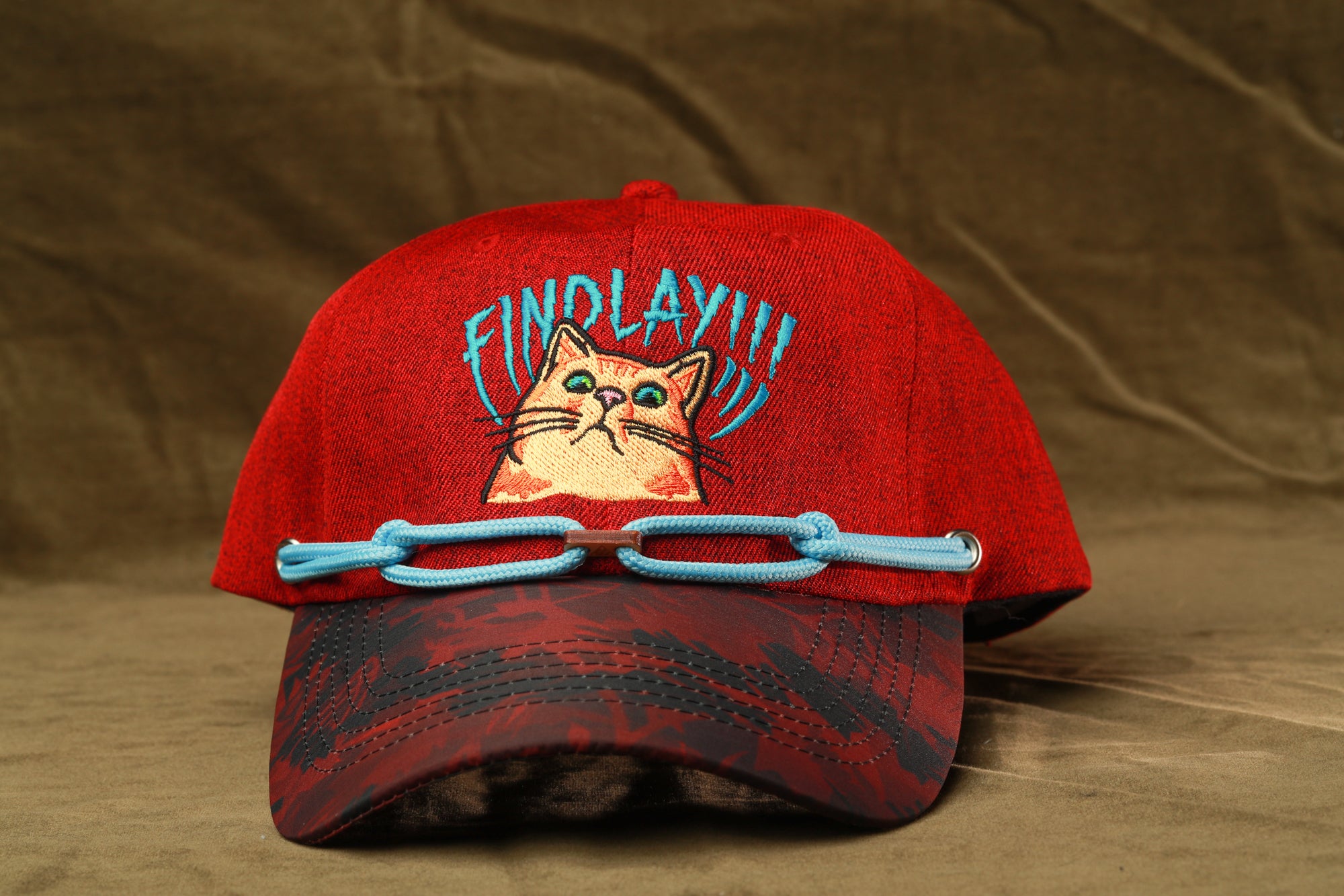 A red baseball cap with a cat design and the text "FIND LAY" printed on it.