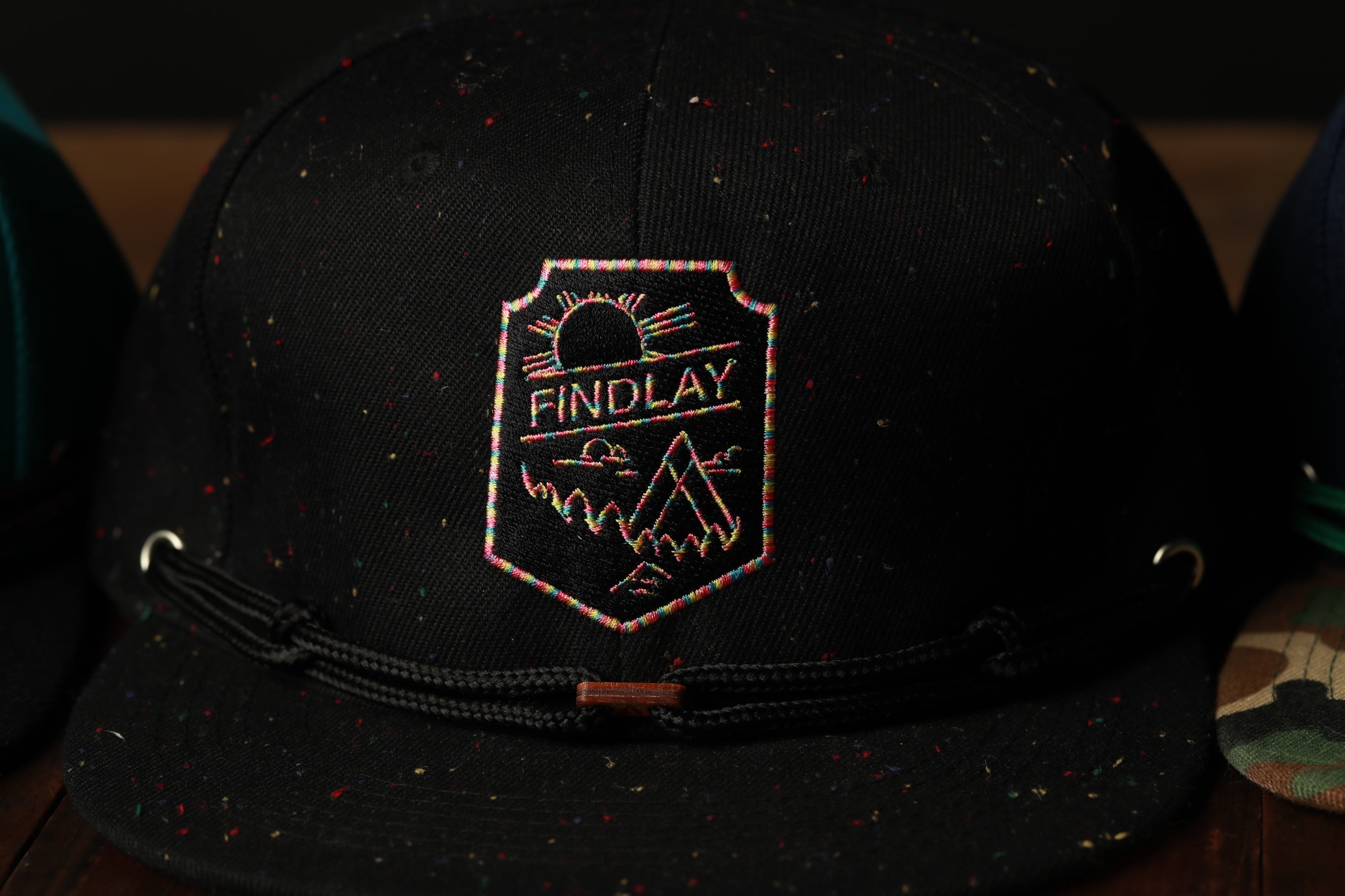 A close-up view of a black baseball cap with a colorful, embroidered logo on the front.