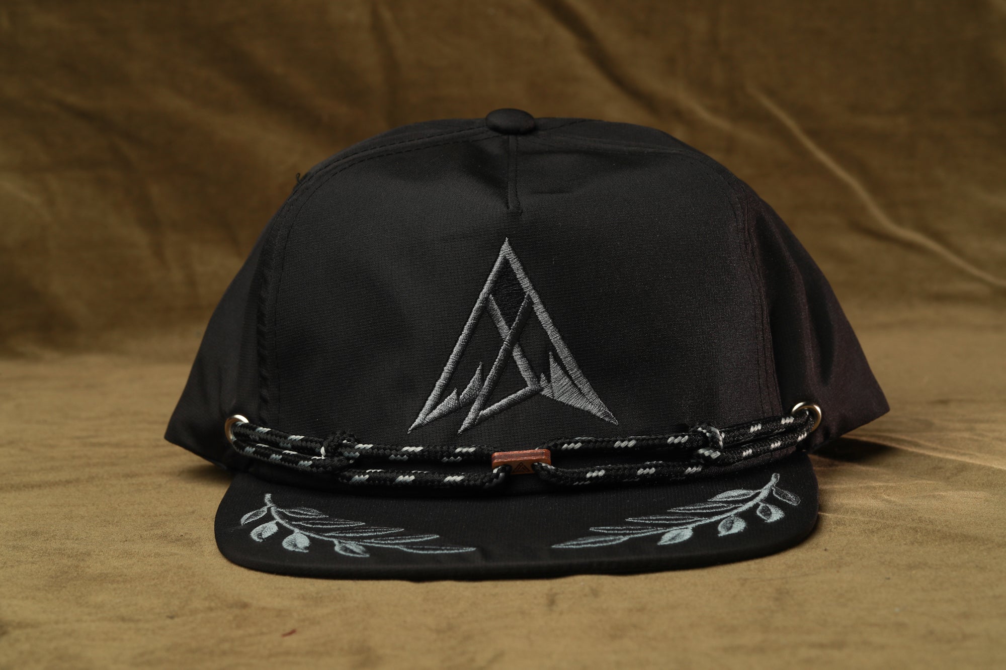 A black baseball cap with a white triangle logo on the front and a black lace-like band around the brim.
