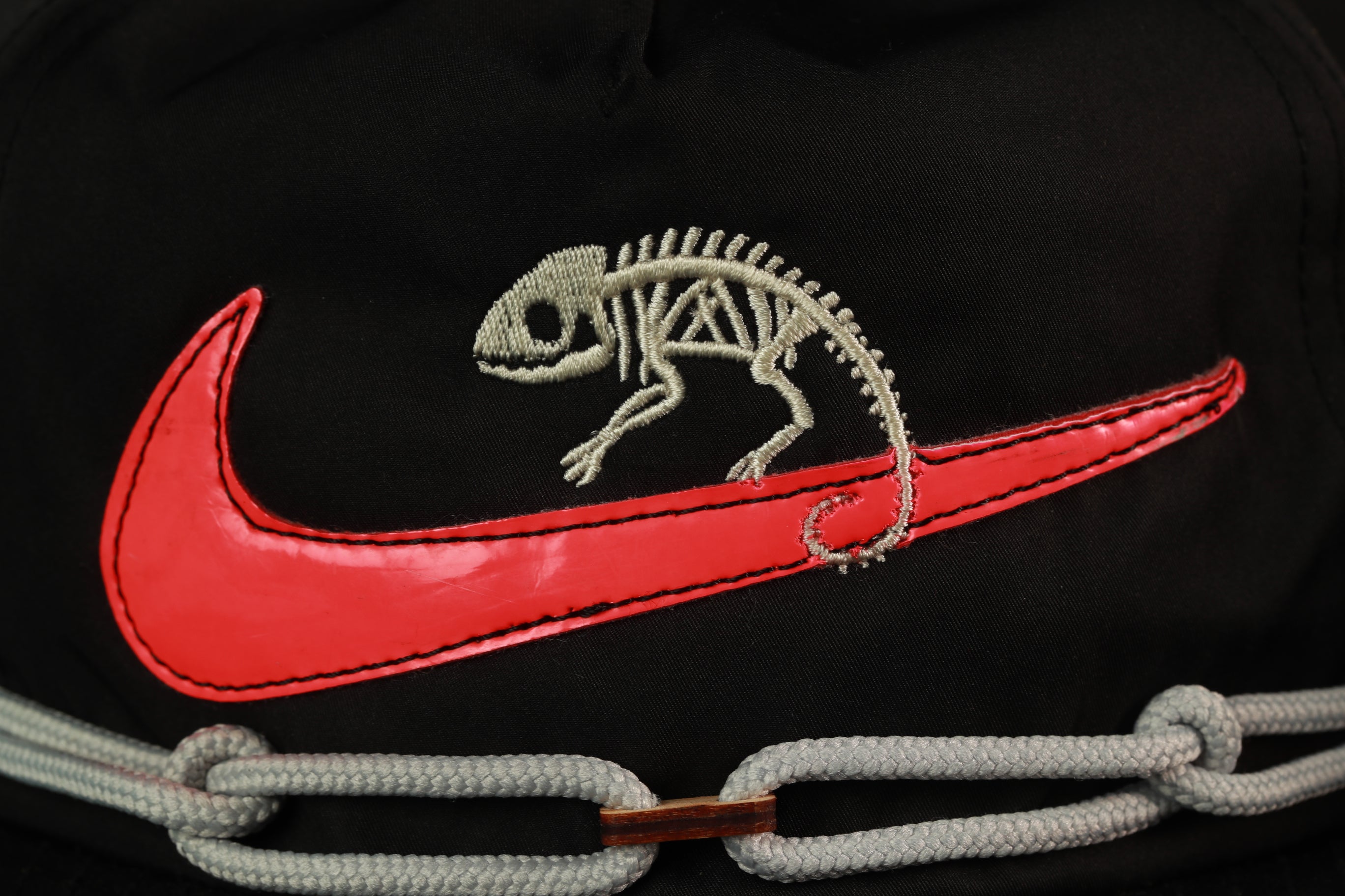 A close-up of a black hat with a red Nike swoosh and a chameleon skeleton embroidered on it.