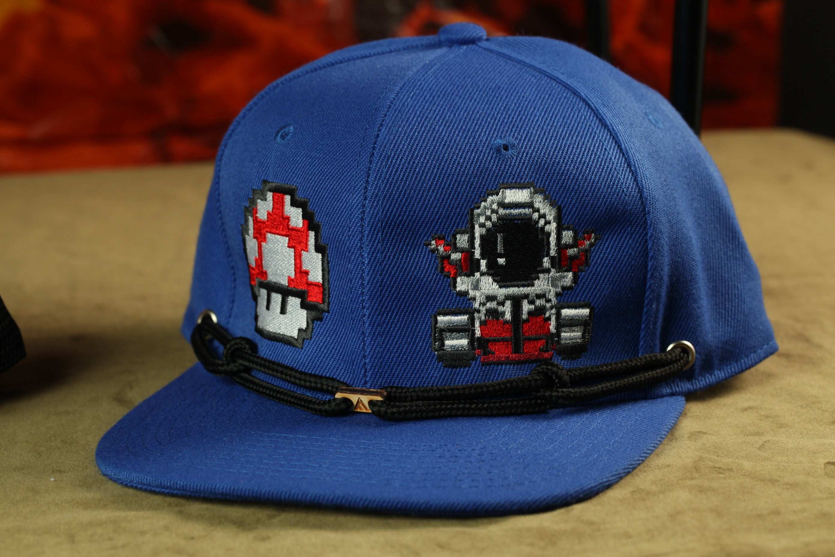 A blue baseball cap with a pixelated design of a mushroom and a space suit on the front.