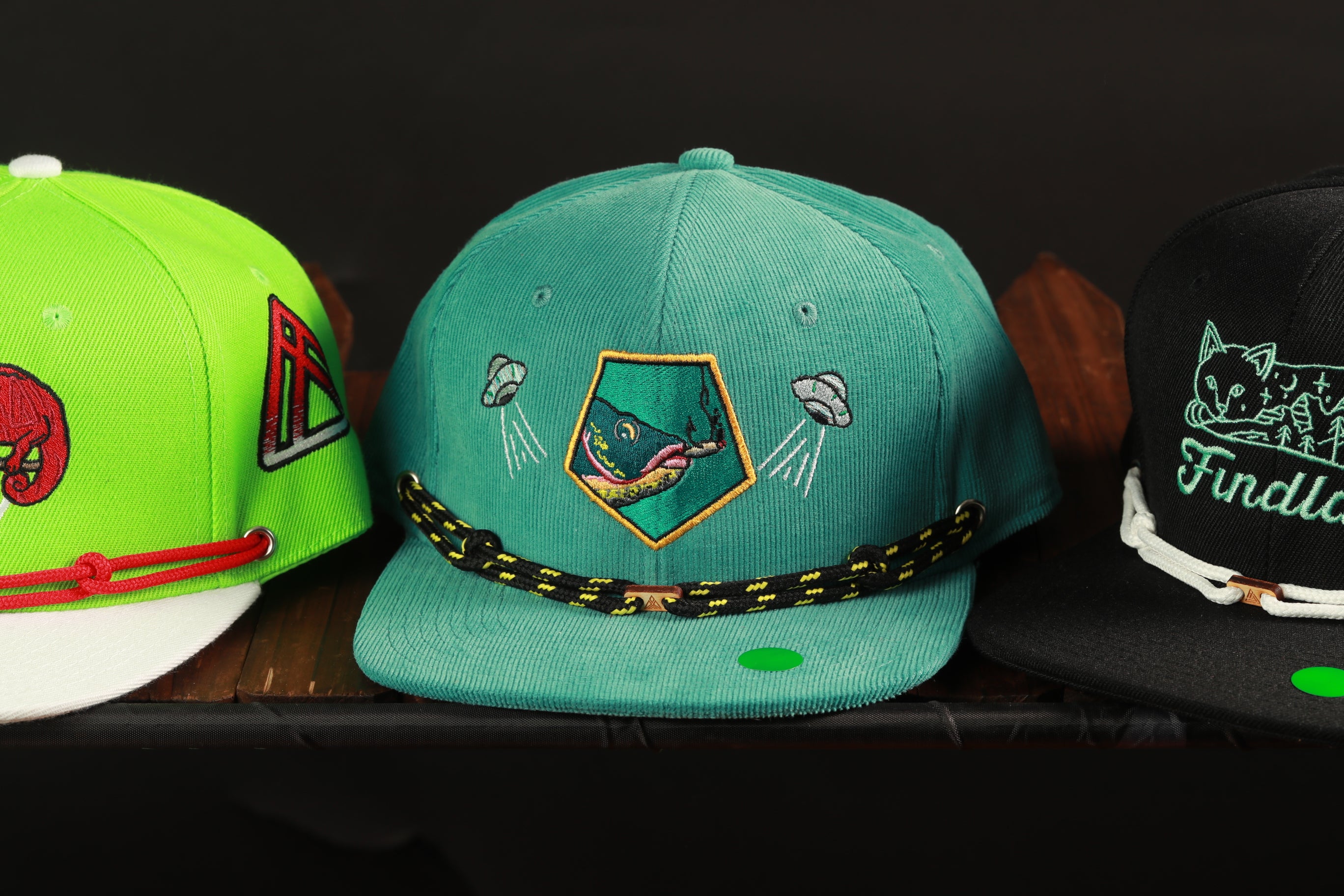 Three colorful baseball caps are displayed on a shelf, each with unique designs and patterns.