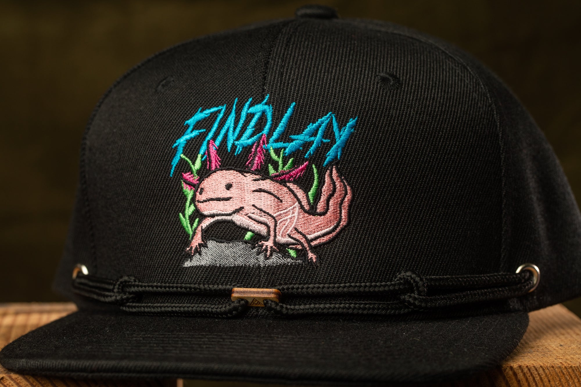 A black baseball cap with a colorful embroidered design featuring a pink salamander or lizard-like creature.