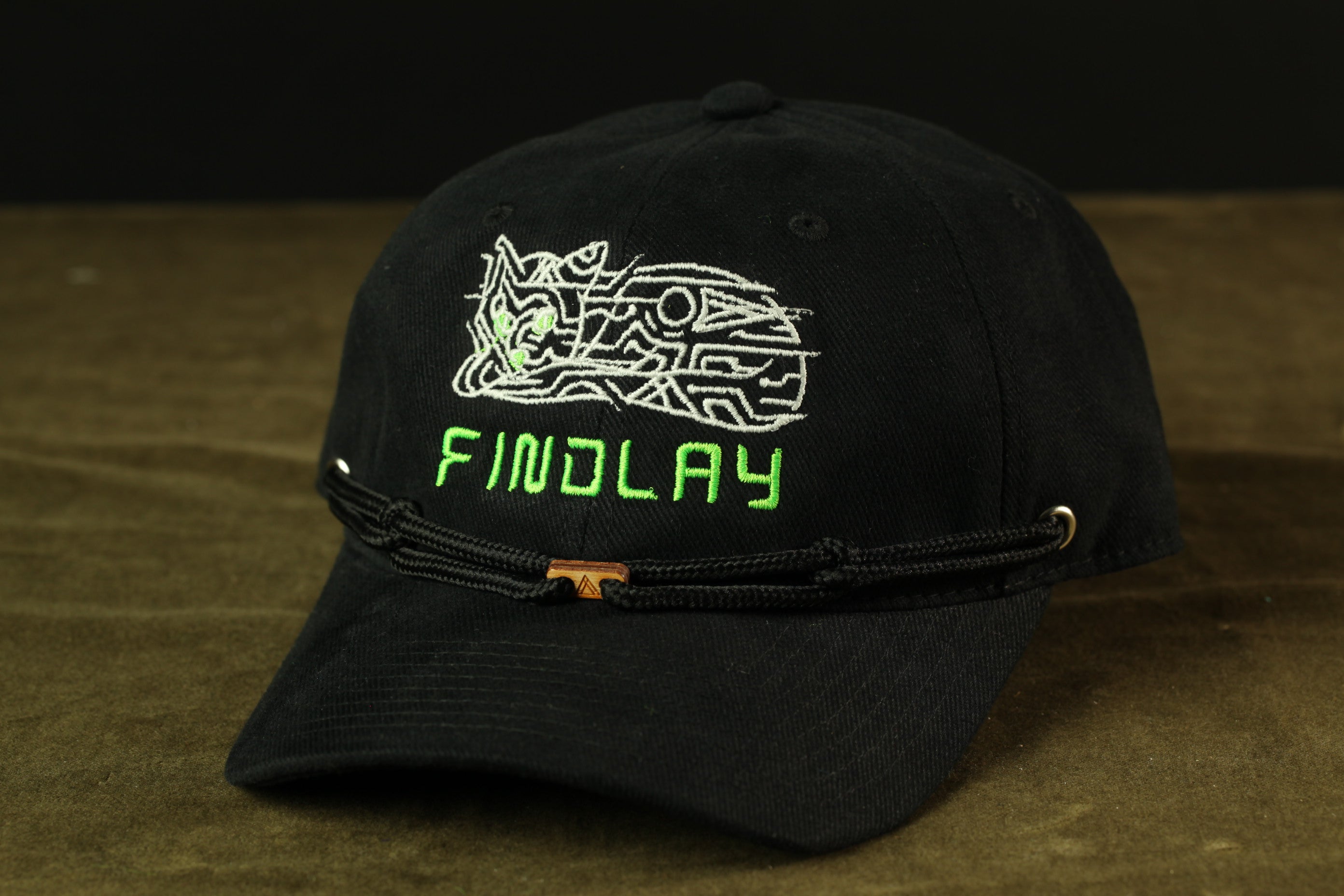 A black baseball cap with a green and white embroidered design and the word "FINDlay" printed on it.