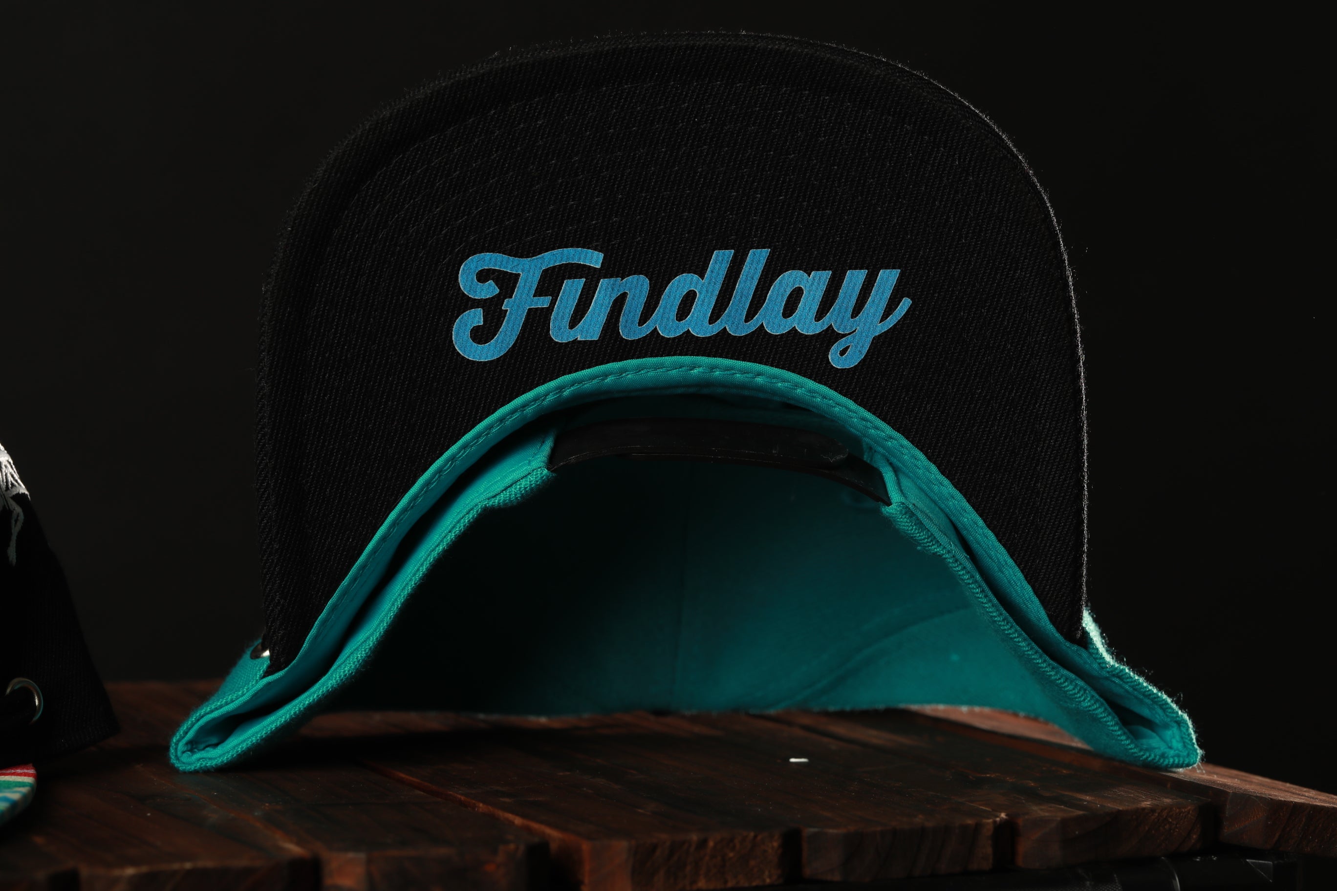 A black baseball cap with a teal interior, featuring the word "Findlay" printed on it.