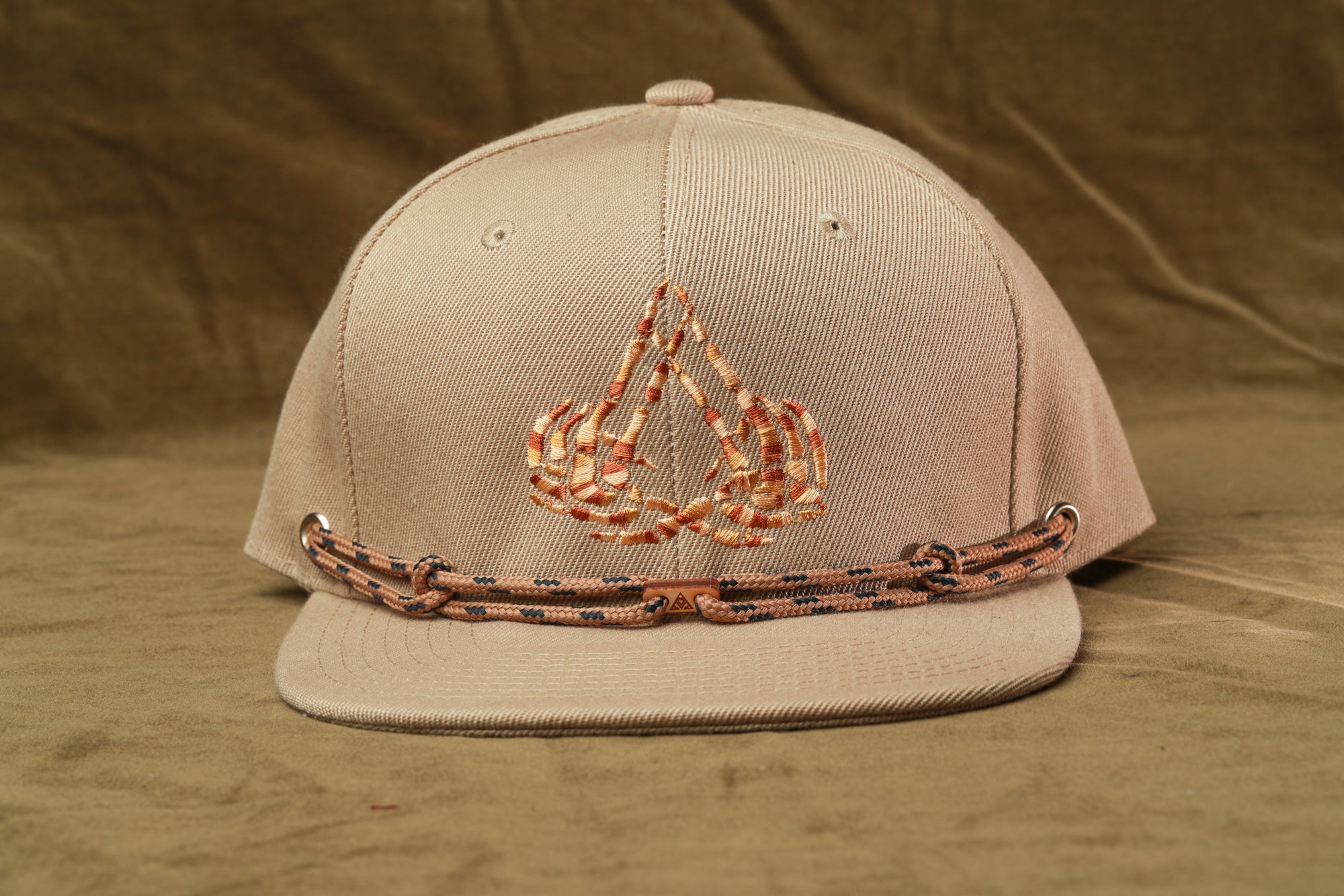 A beige baseball cap with a decorative logo on the front, featuring a pair of crossed fingers.