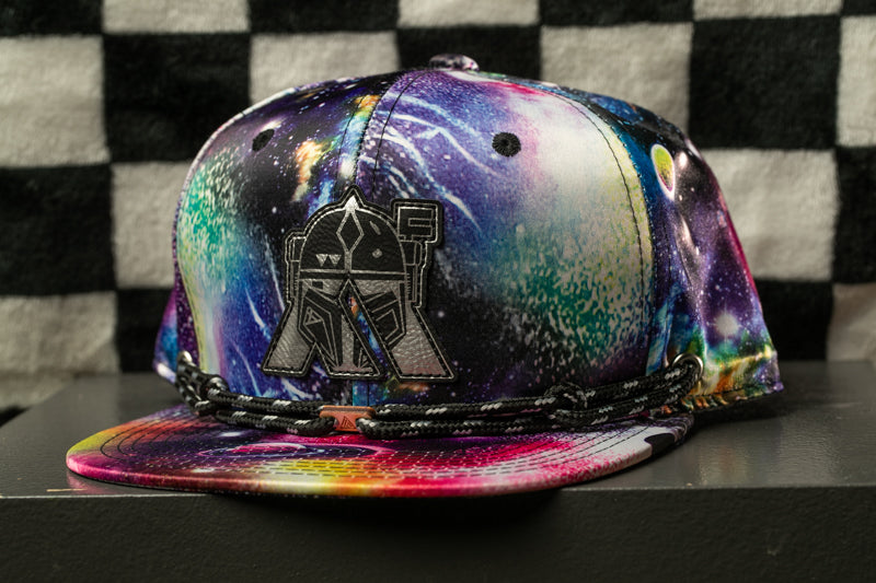 A colorful, patterned baseball cap with a space-themed design, featuring a helmet-like emblem on the front.