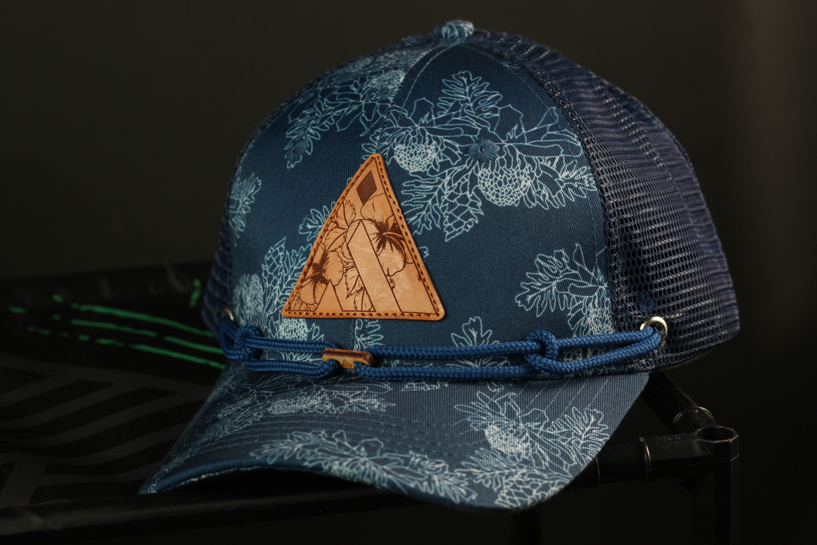 A blue and white floral patterned baseball cap with a leather patch and blue string.