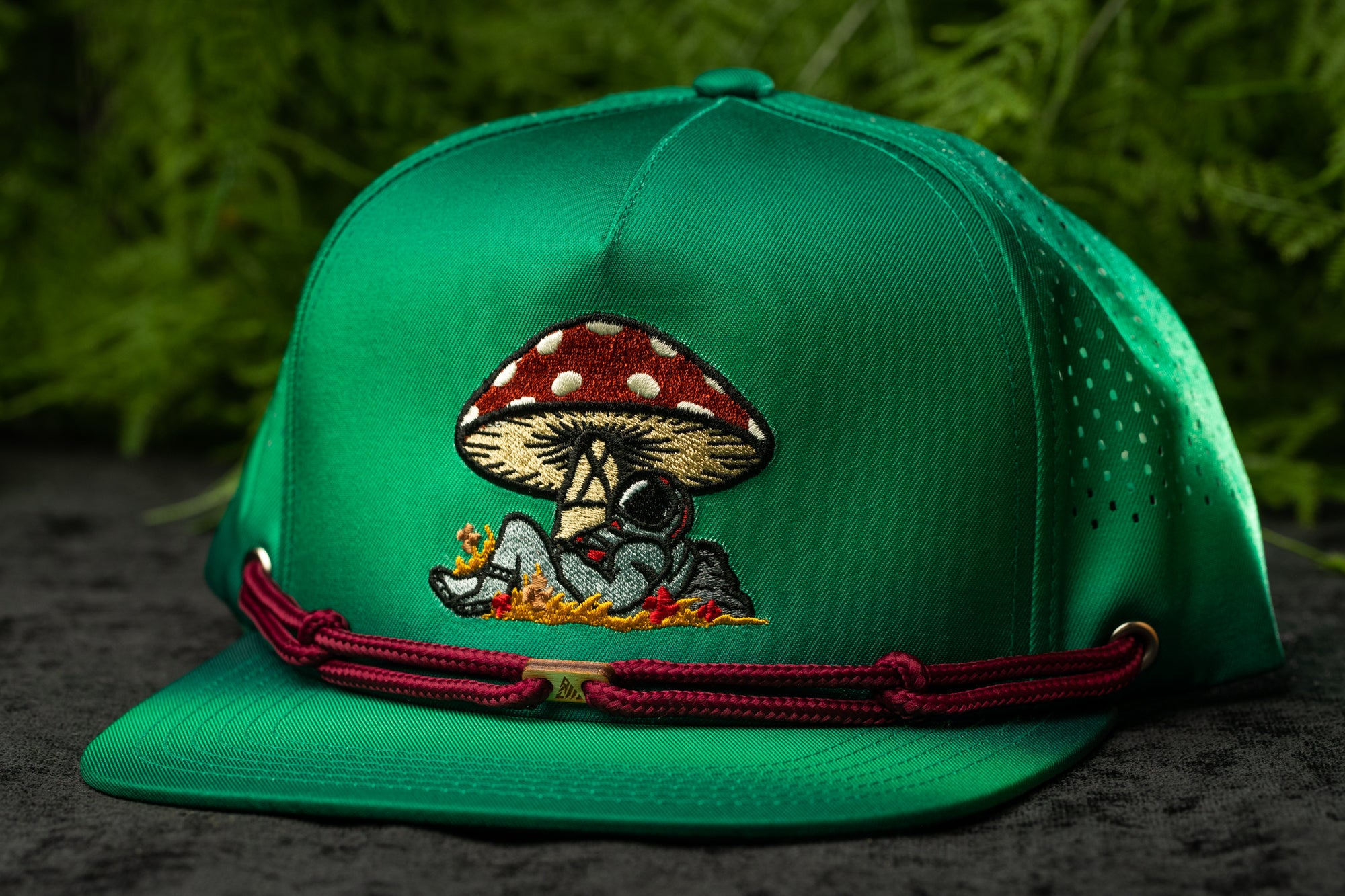 A green baseball cap with a mushroom design and a red string around the brim.