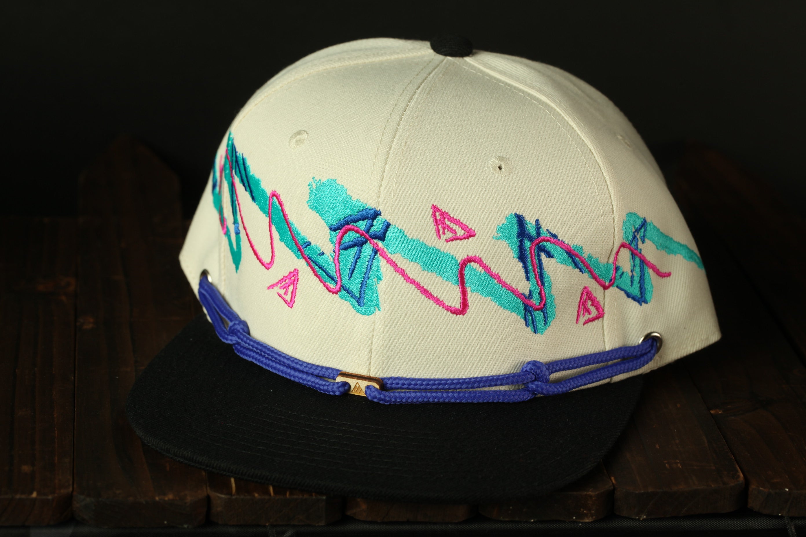 A white baseball cap with a black brim and a colorful, abstract design on the front.