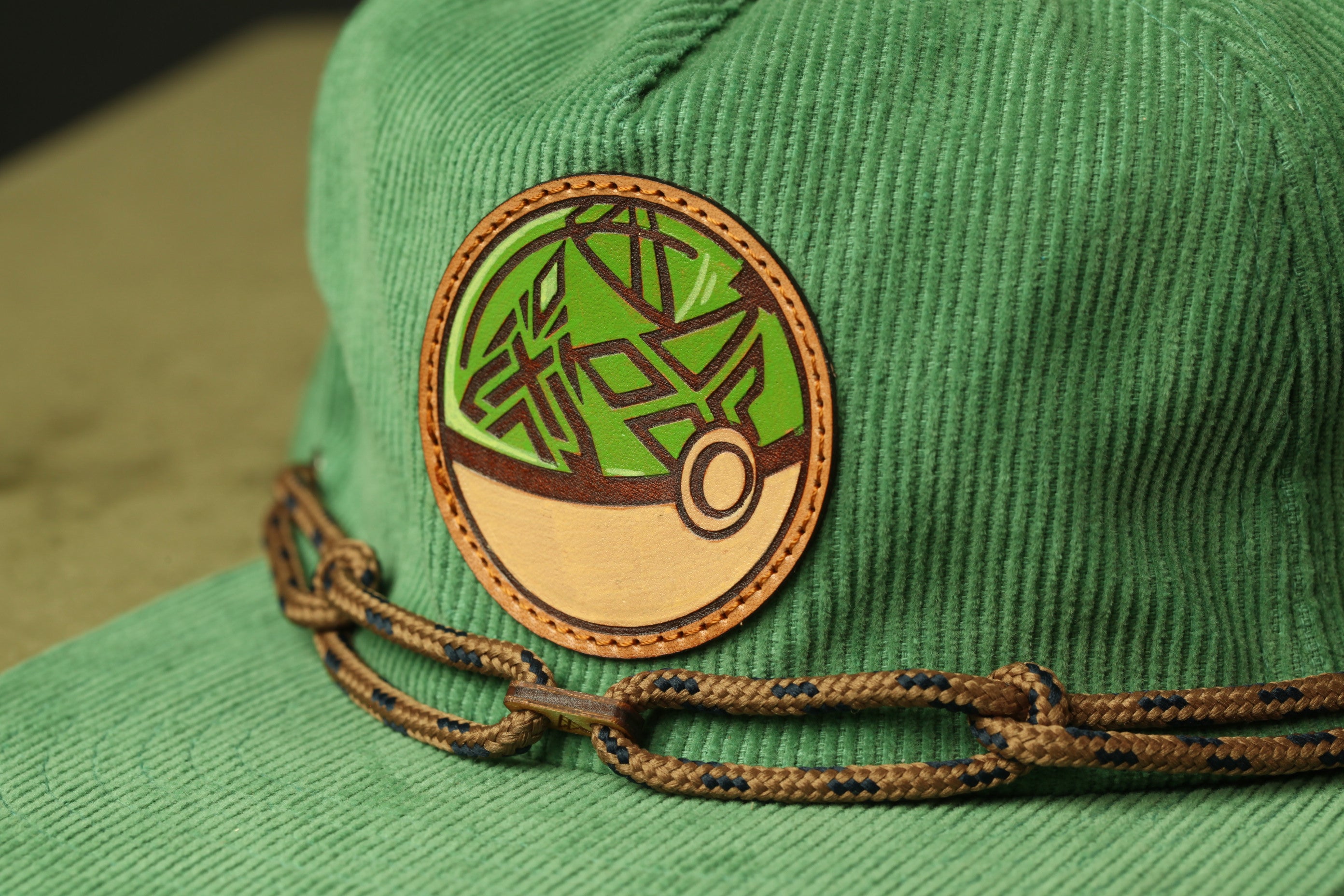 A close-up view of a green baseball cap with a circular patch featuring a geometric design.