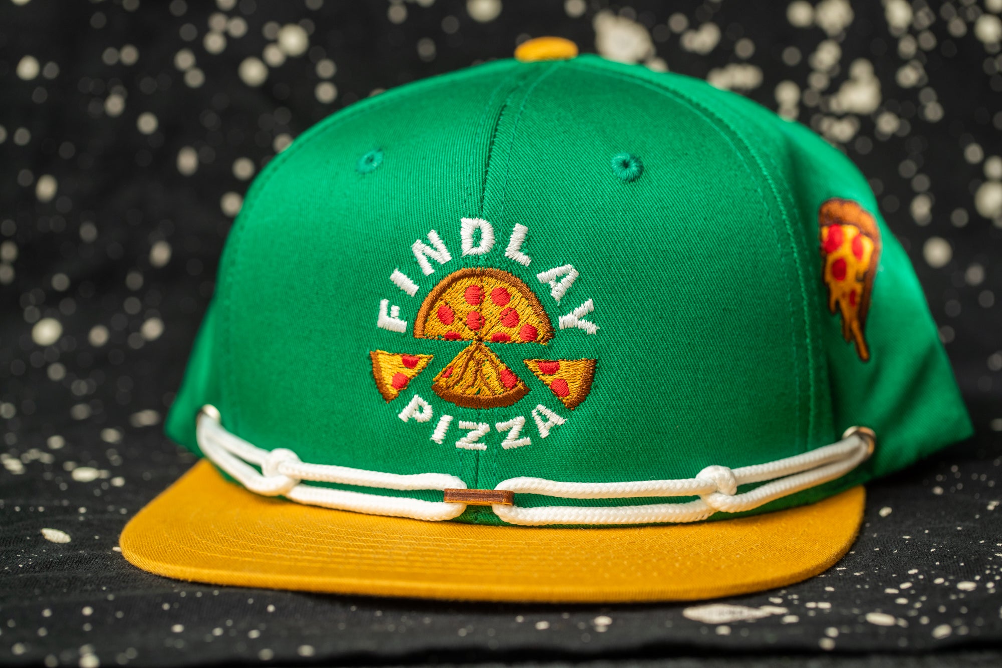 A green baseball cap with a yellow brim, featuring a logo for "Findlay Pizza".