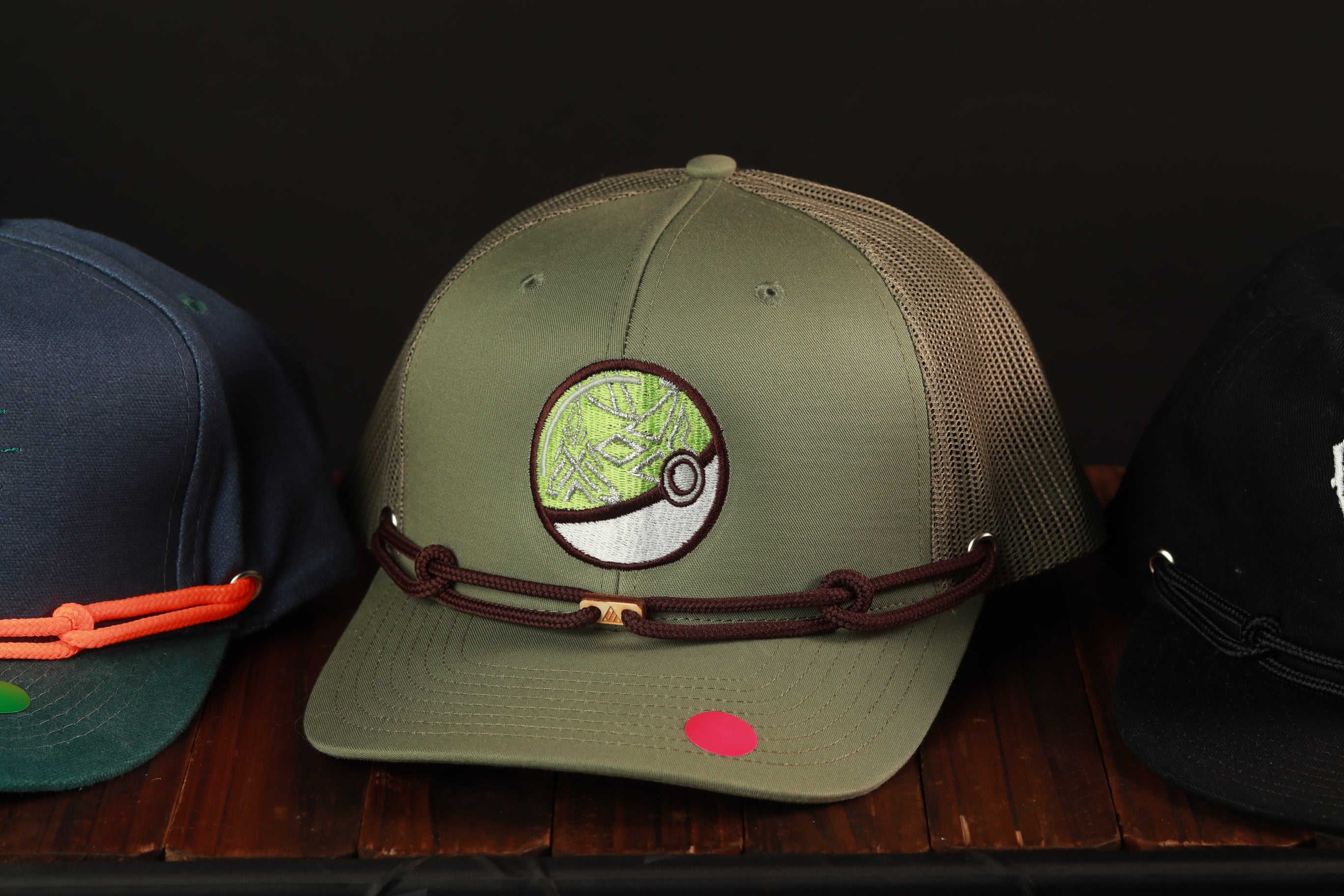 A collection of baseball caps with various designs, including a green cap with a circular patch and a brown cap with a black and white pattern.