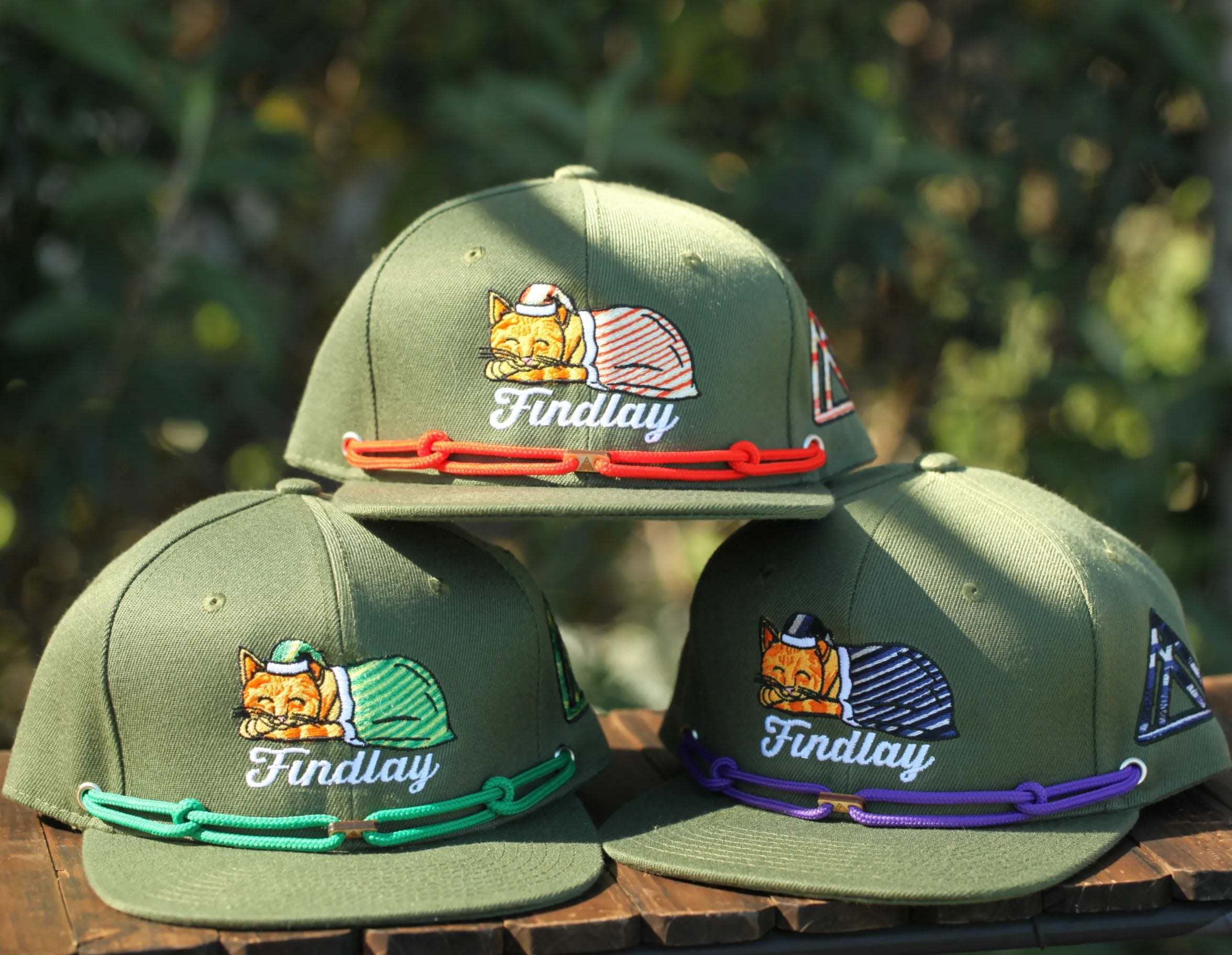 A collection of green baseball caps with the word "Findlay" printed on them, arranged on a wooden surface.