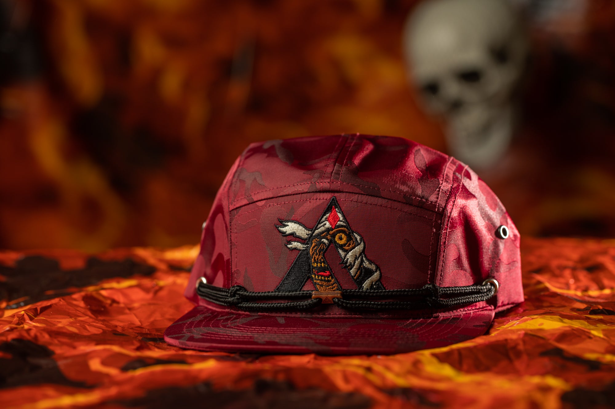 A red baseball cap with a graphic design on it, placed on a red and orange patterned surface.