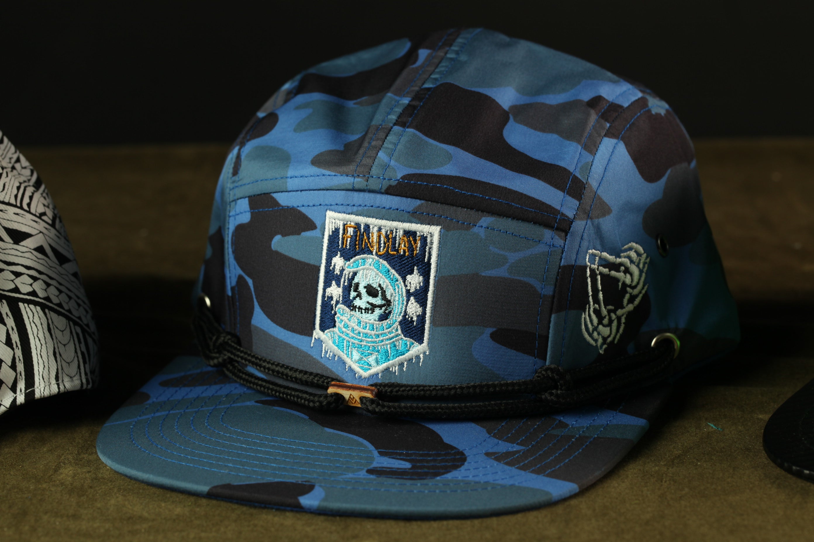 A camouflage baseball cap with a skull and crossbones design, featuring a patch with the text "FINISH" on the front.