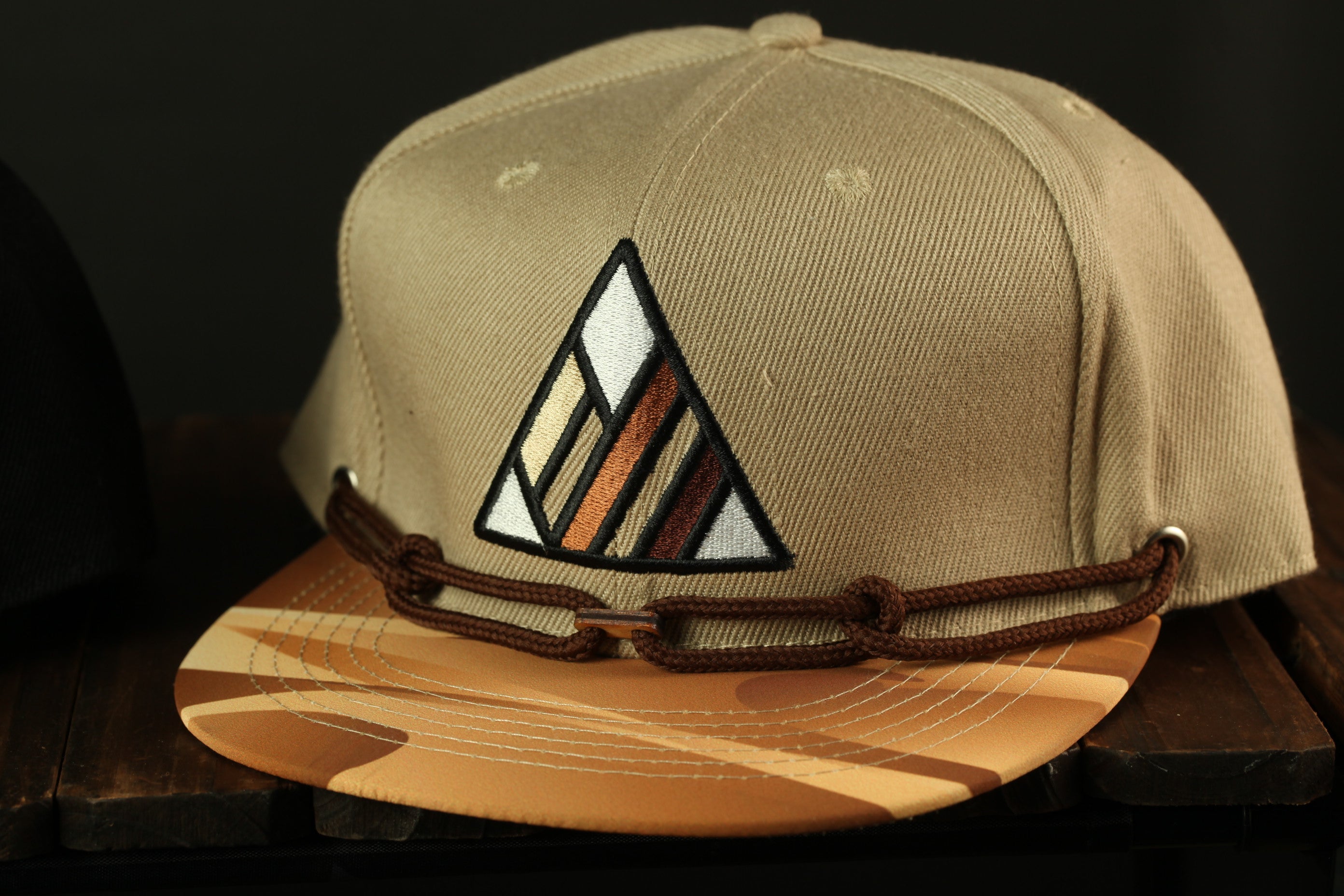 A beige baseball cap with a geometric pattern on the front, featuring a triangle design with horizontal and vertical stripes.