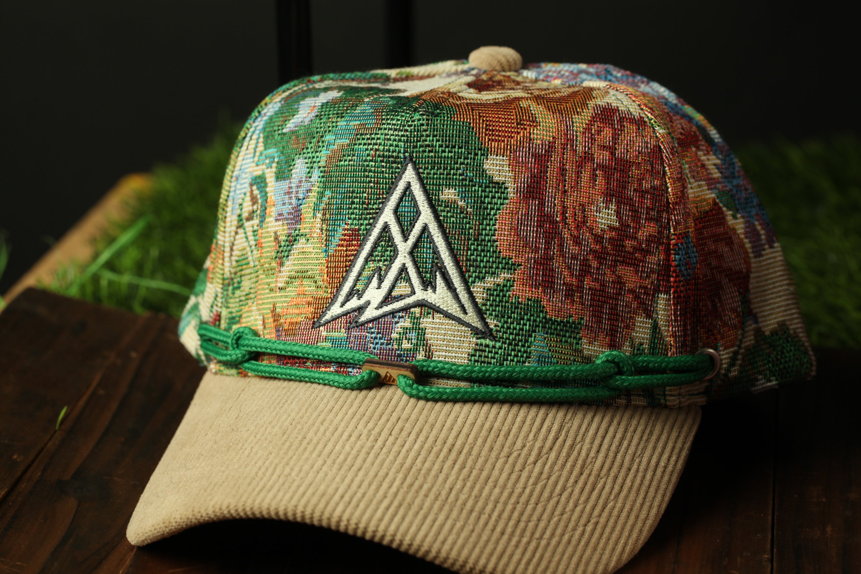 A colorful, patterned baseball cap with a green band and a white logo on the front, sitting on a wooden surface.