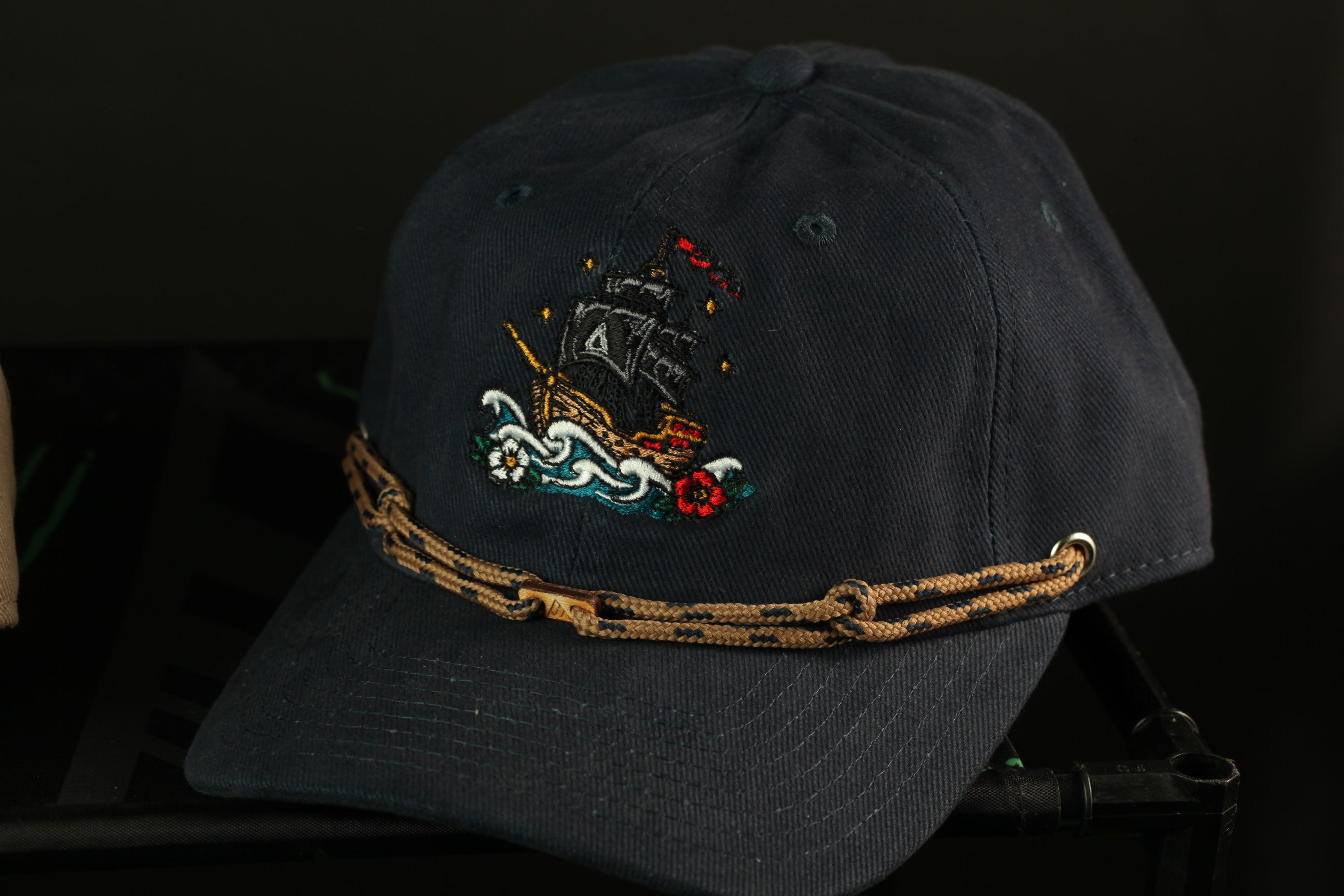 A navy blue baseball cap with a decorative embroidered design of a ship on the front.