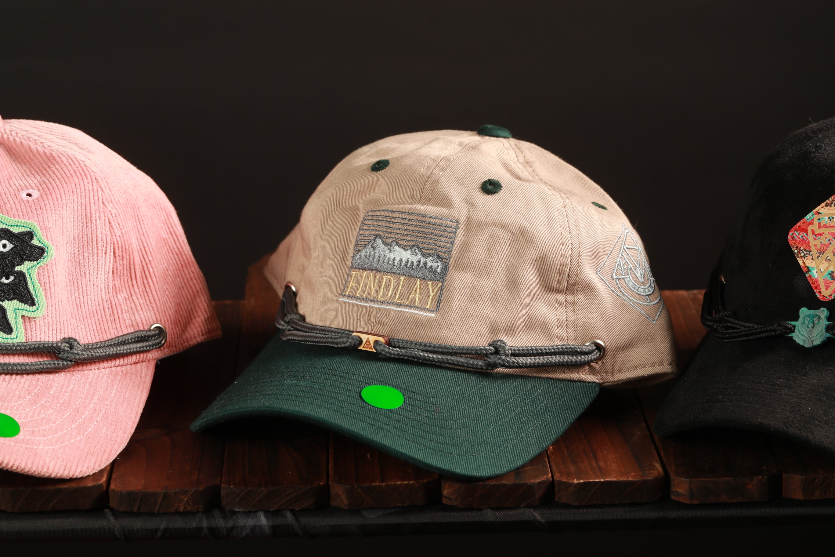 Three baseball caps are displayed on a wooden surface, each with different colors and designs.