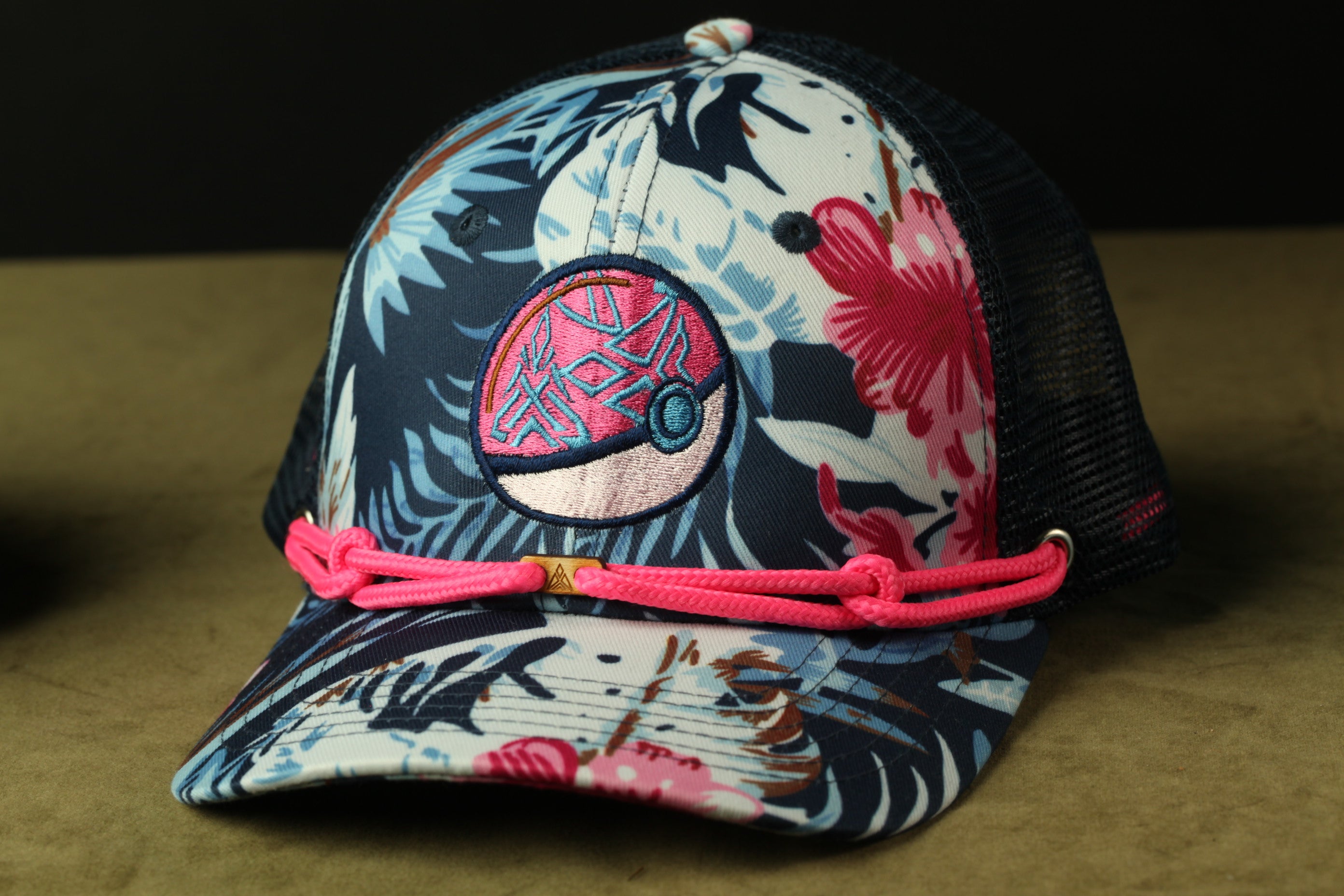 A colorful baseball cap with a floral pattern and a Pokemon-inspired design, featuring a pink braided strap.