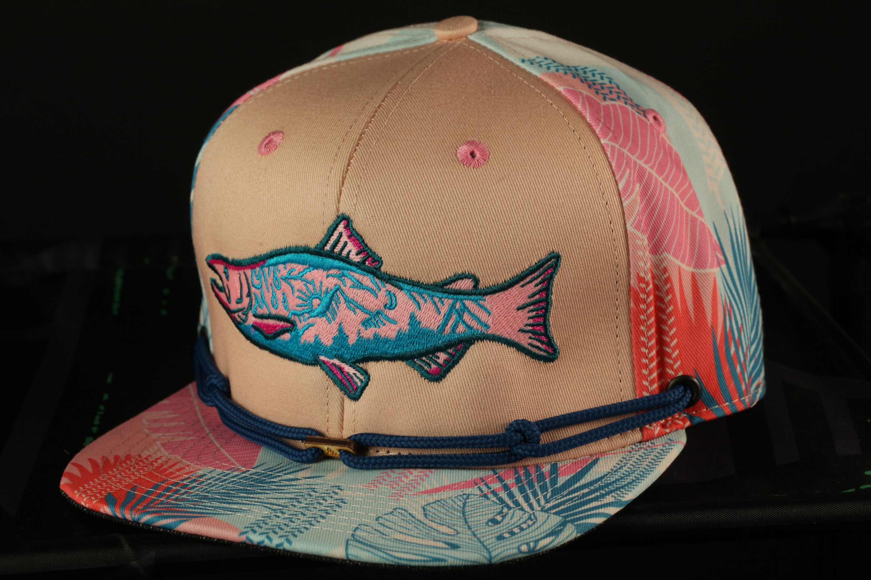 A colorful baseball cap with a fish embroidered on it, featuring a tropical leaf pattern.