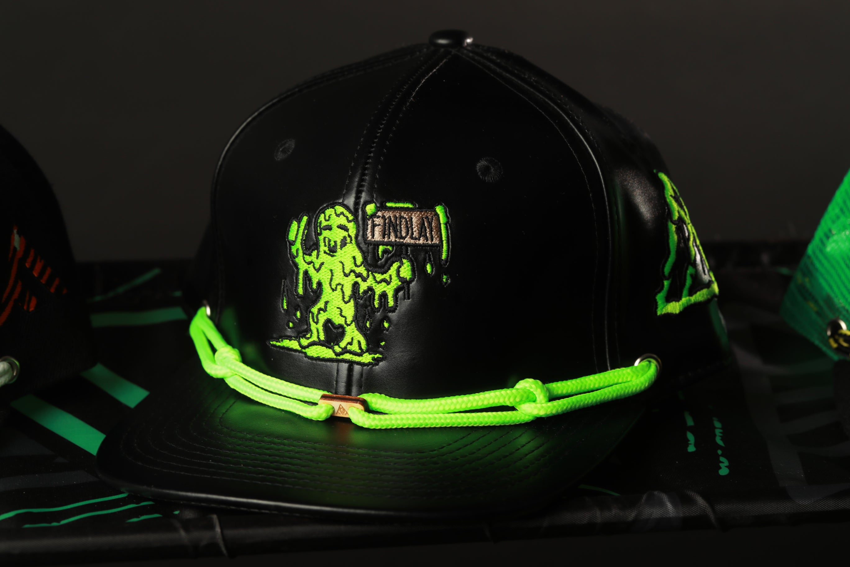 A black baseball cap with a green glow, featuring a graphic of a green alien-like creature on the front.