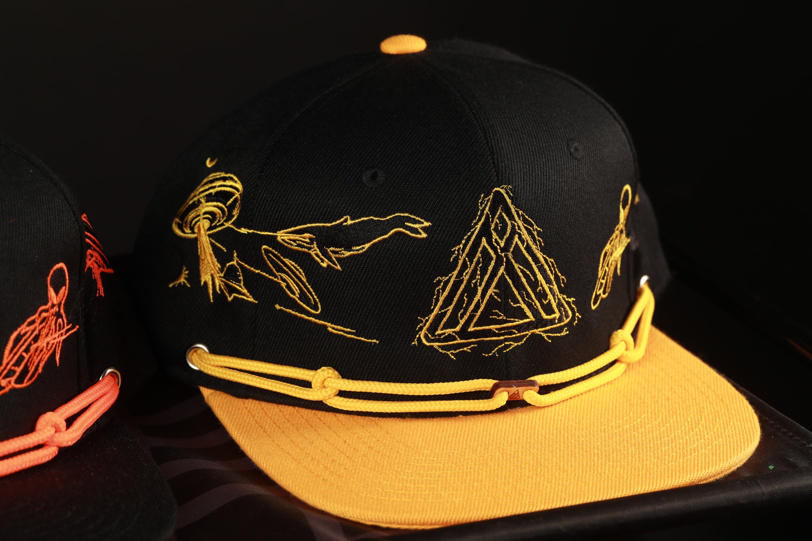 A black baseball cap with yellow embroidered designs on the front, including a triangle and a bird-like figure.