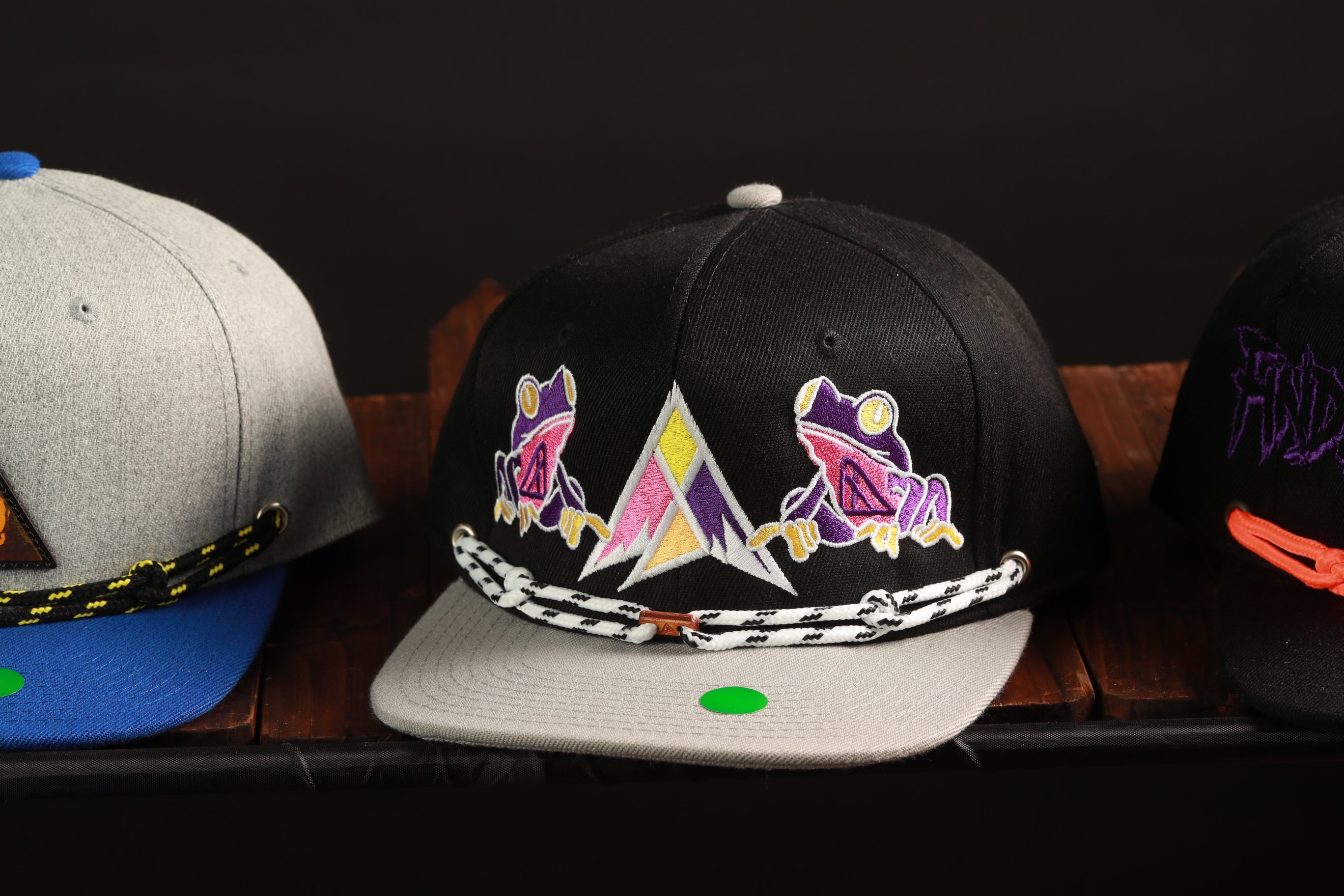 Three baseball caps with different designs and colors are displayed on a wooden surface.