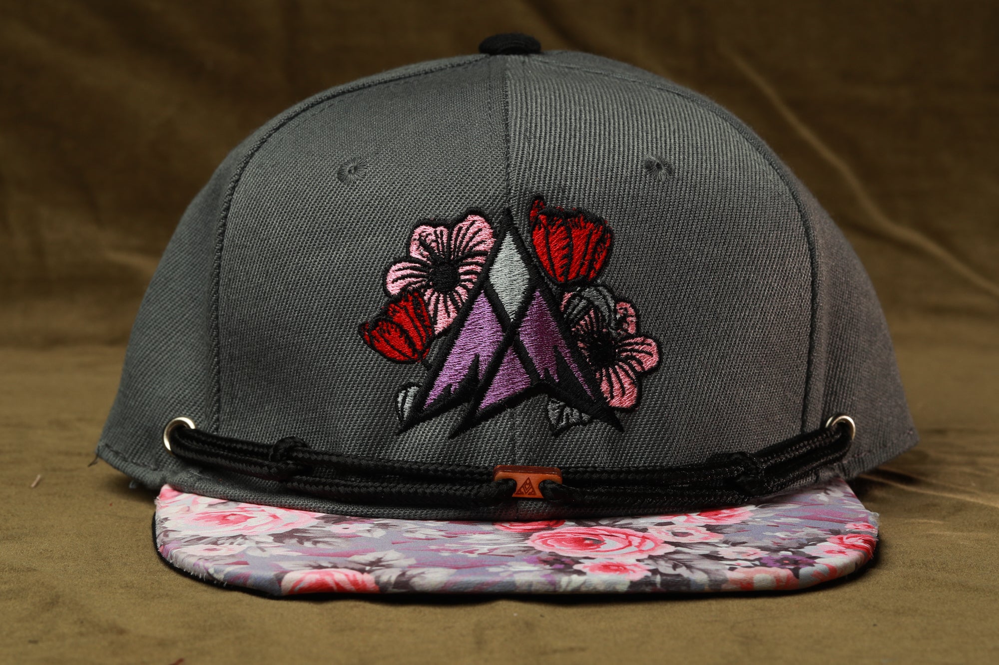 A gray baseball cap with a floral pattern and a black strap.