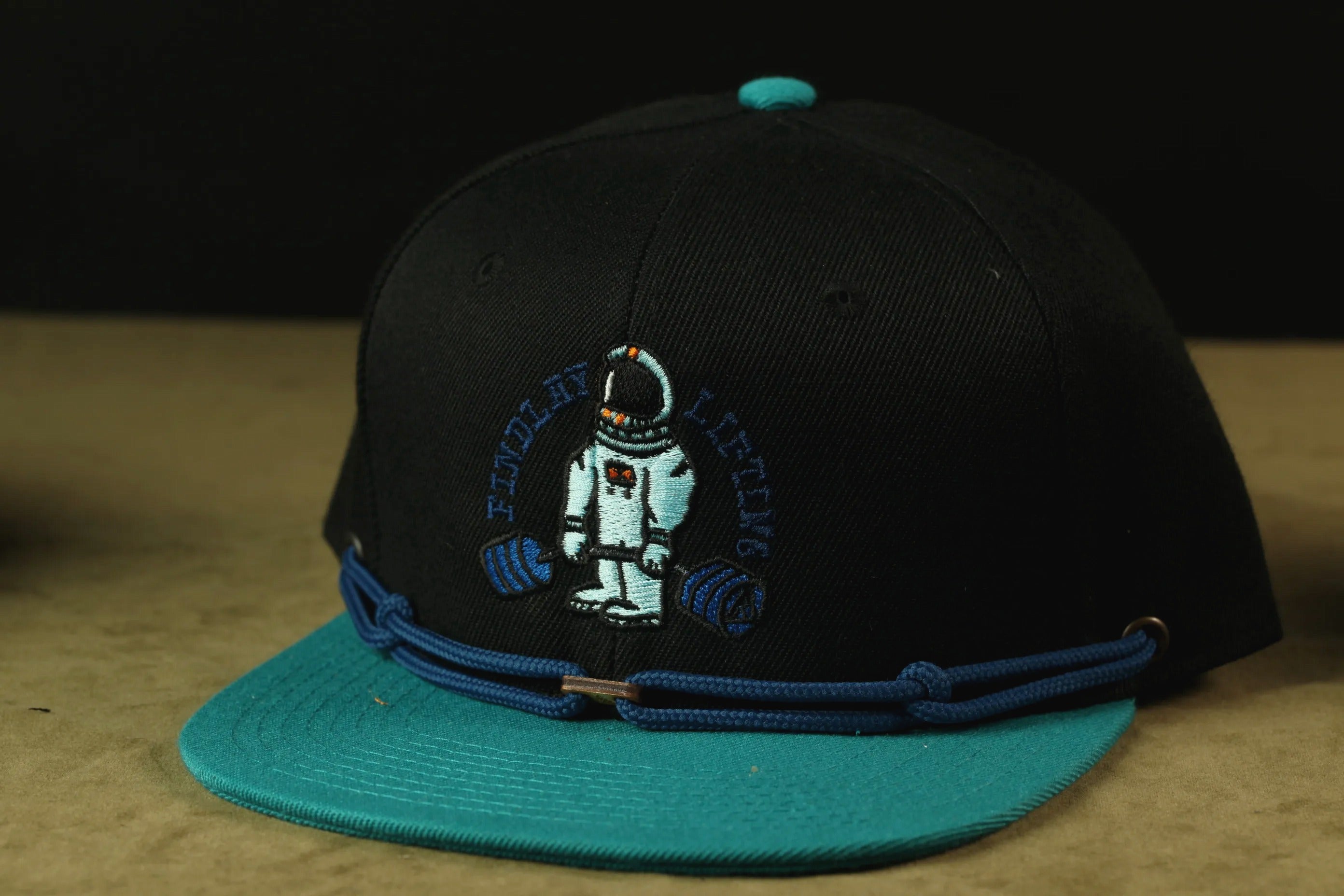 A black baseball cap with a blue brim and a graphic of an astronaut on the front.
