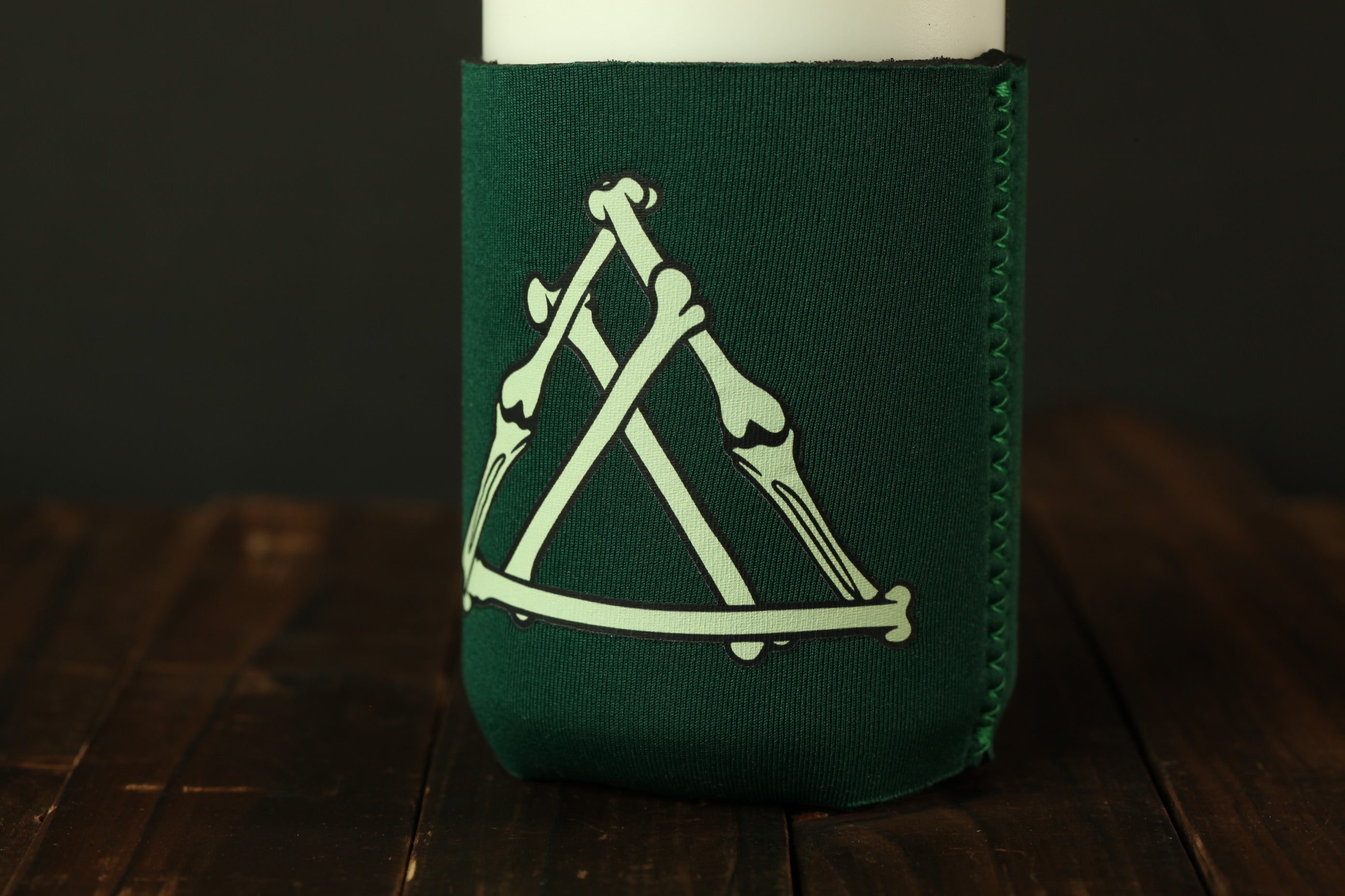 A green thermal cup sleeve with a white graphic design on it, placed on a wooden surface.