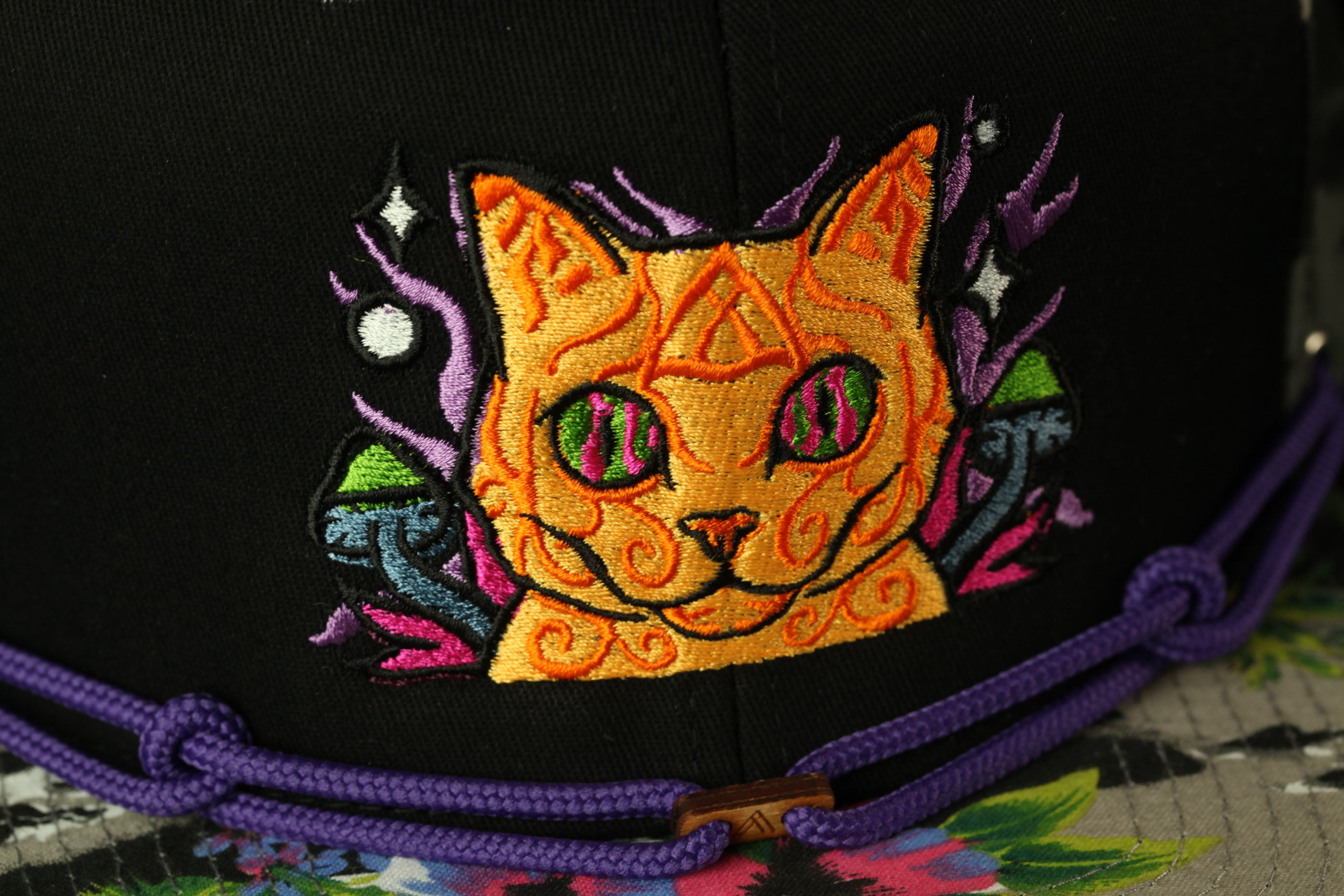 a close-up view of a black baseball cap with a colorful, embroidered cat design on the front.