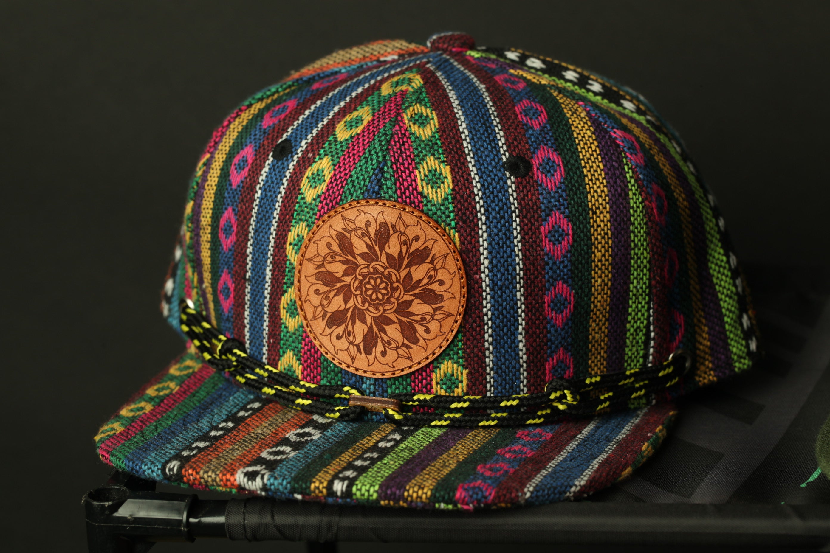 A colorful, patterned baseball cap with a circular leather patch on the front.