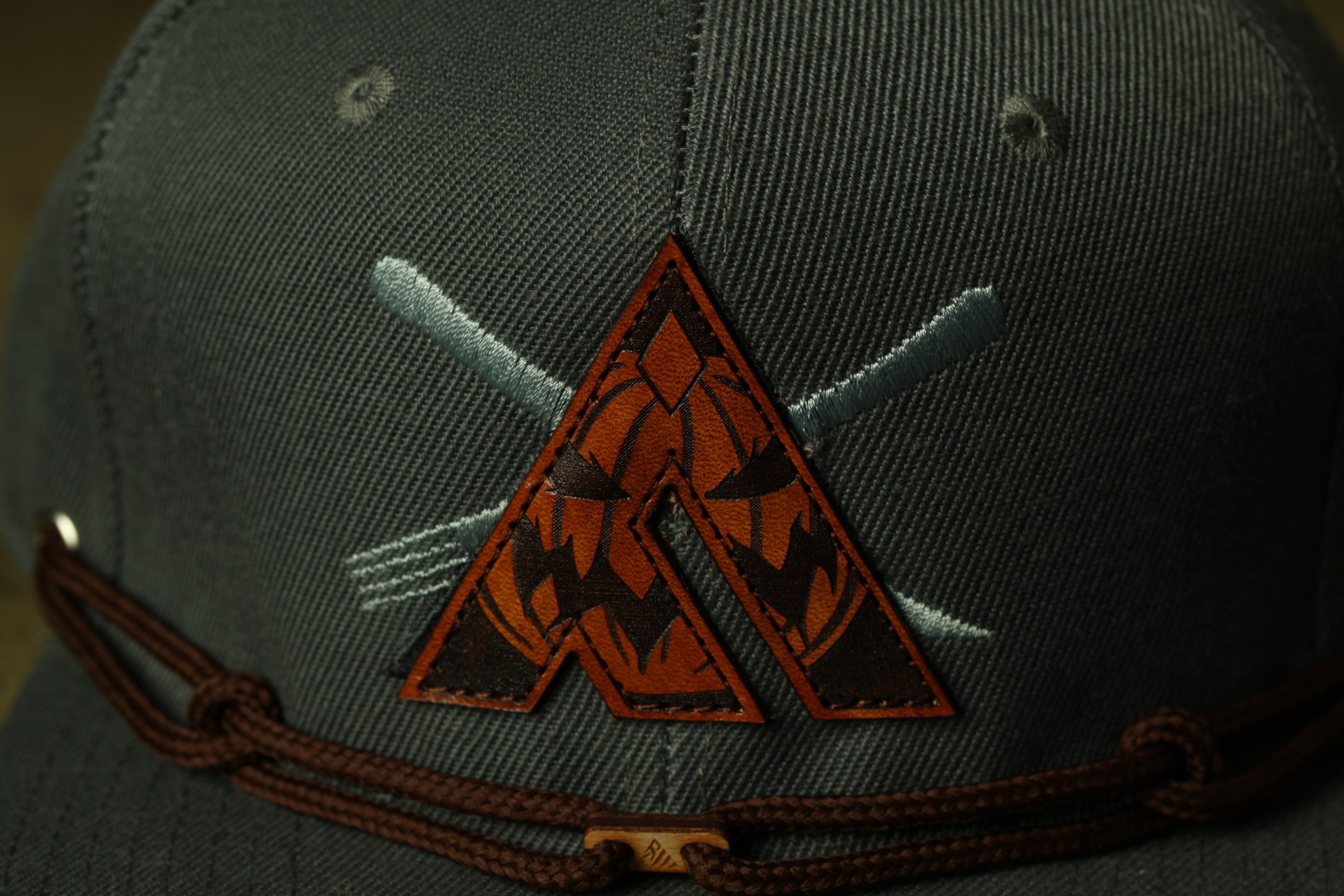 A close-up view of a dark green baseball cap with a brown leather patch featuring an orange triangle design and crossed forks.