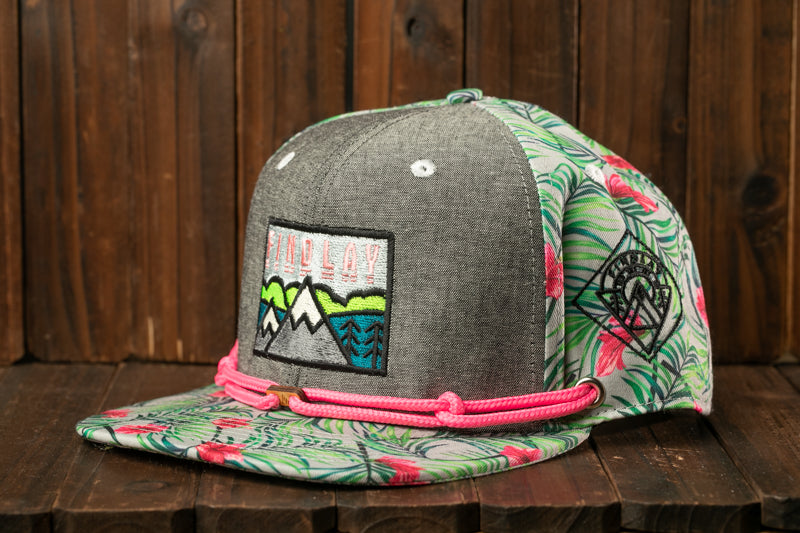 A gray baseball cap with a floral pattern and a small embroidered patch on the front, sitting on a wooden surface.