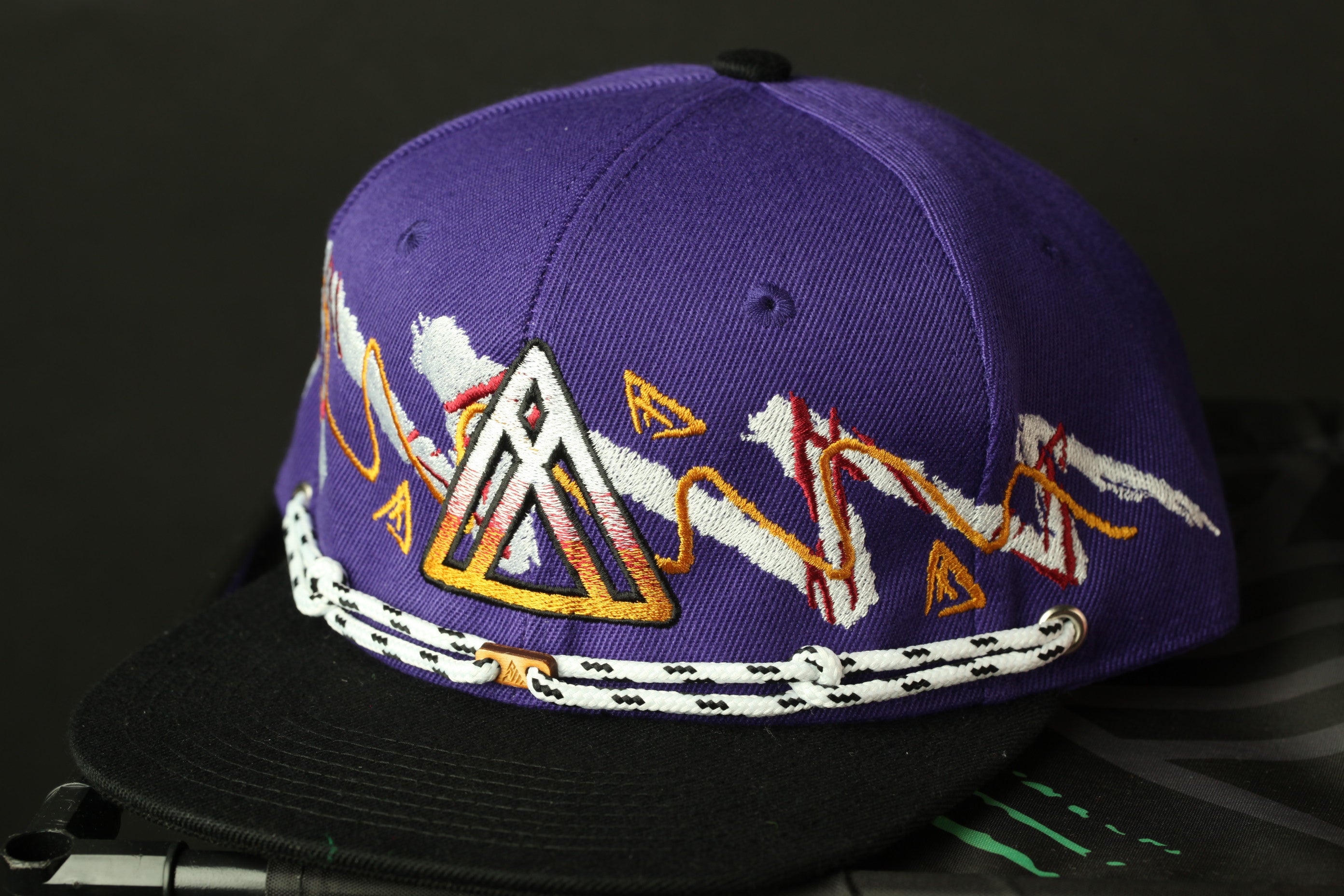 A purple baseball cap with a black brim and white and orange designs on the front.