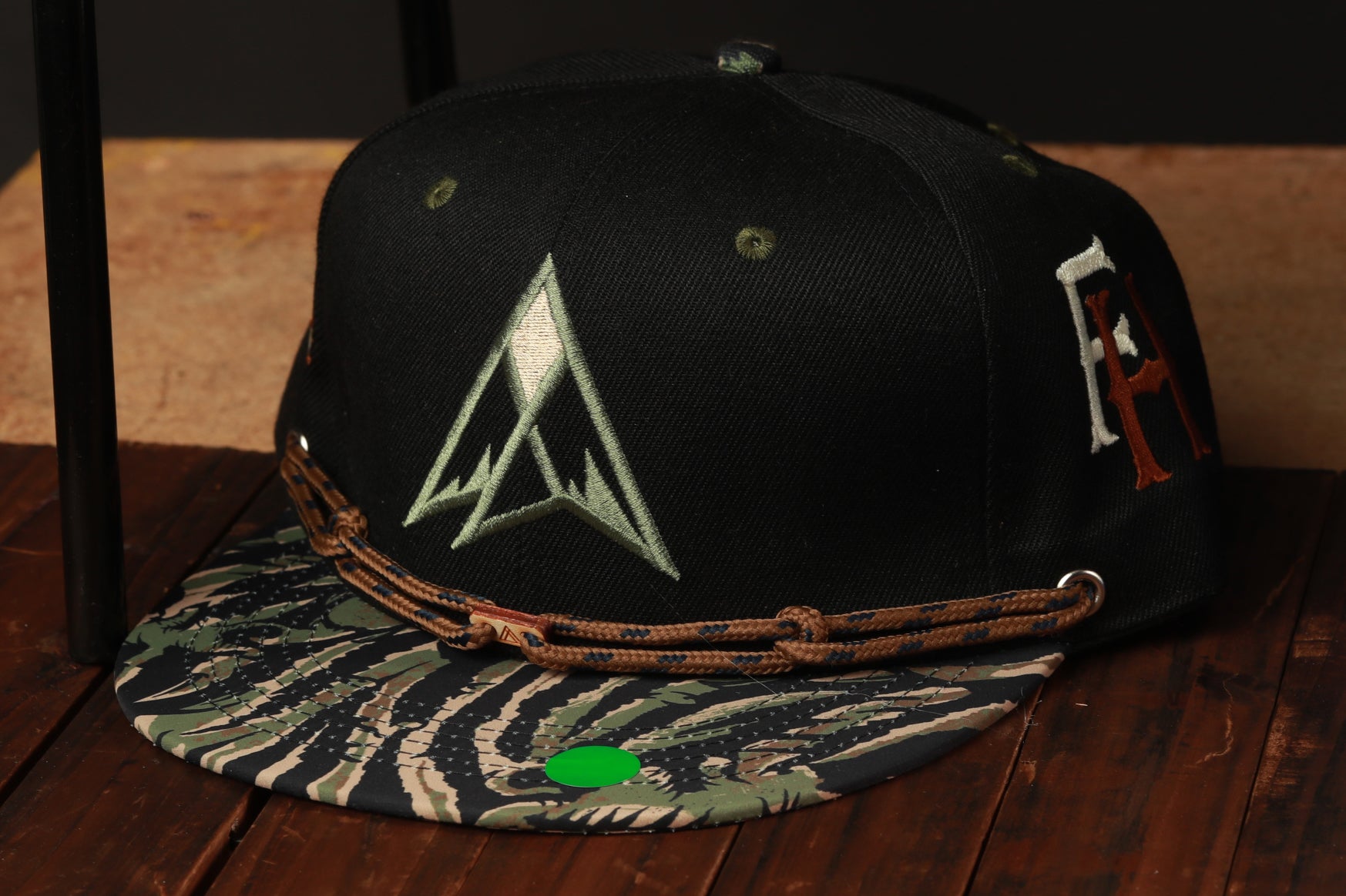 A black baseball cap with a camouflage pattern and a white triangle logo is placed on a wooden surface.