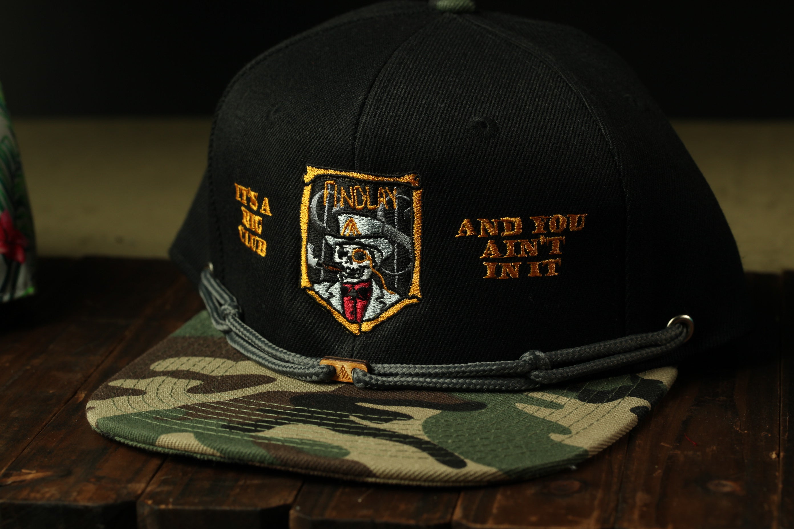 A black baseball cap with a camouflage pattern and an embroidered logo on the front.