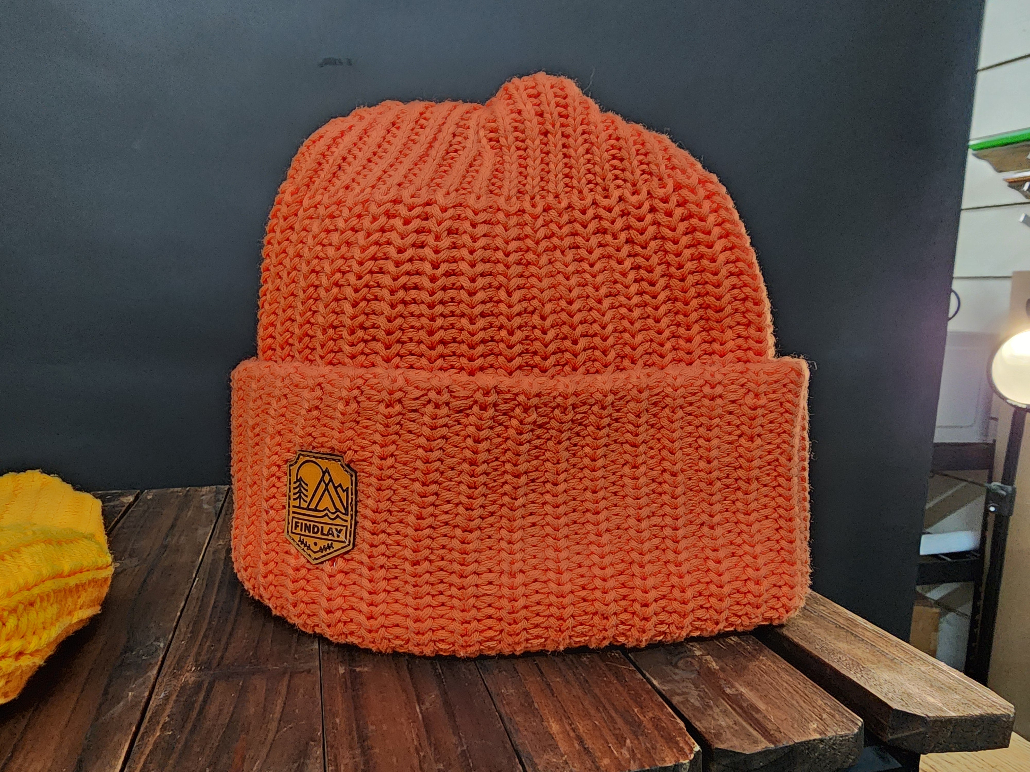 An orange knit beanie with a mountain logo on it, placed on a wooden surface.