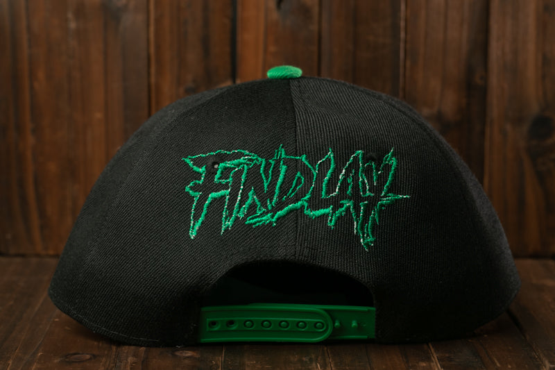 A black baseball cap with green text on it, placed on a wooden surface.