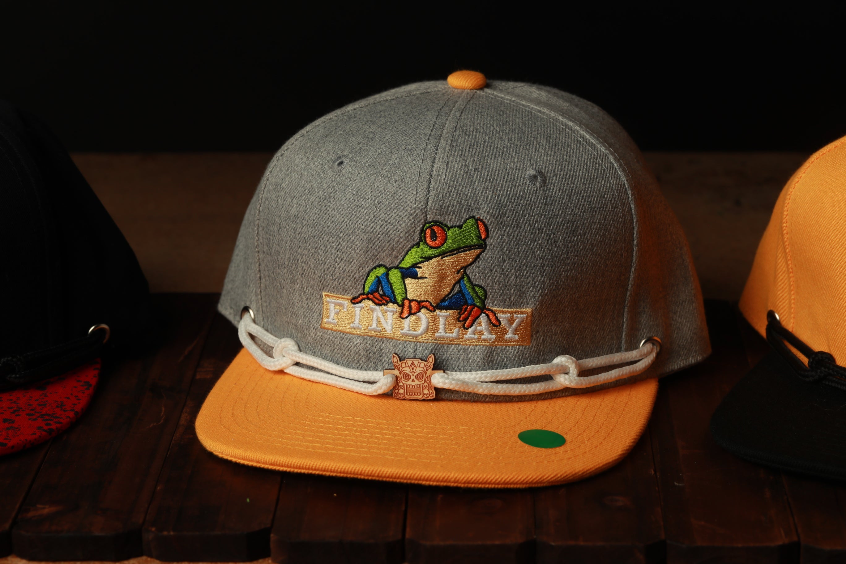 A gray baseball cap with a green frog embroidered on it, sitting on a wooden surface.