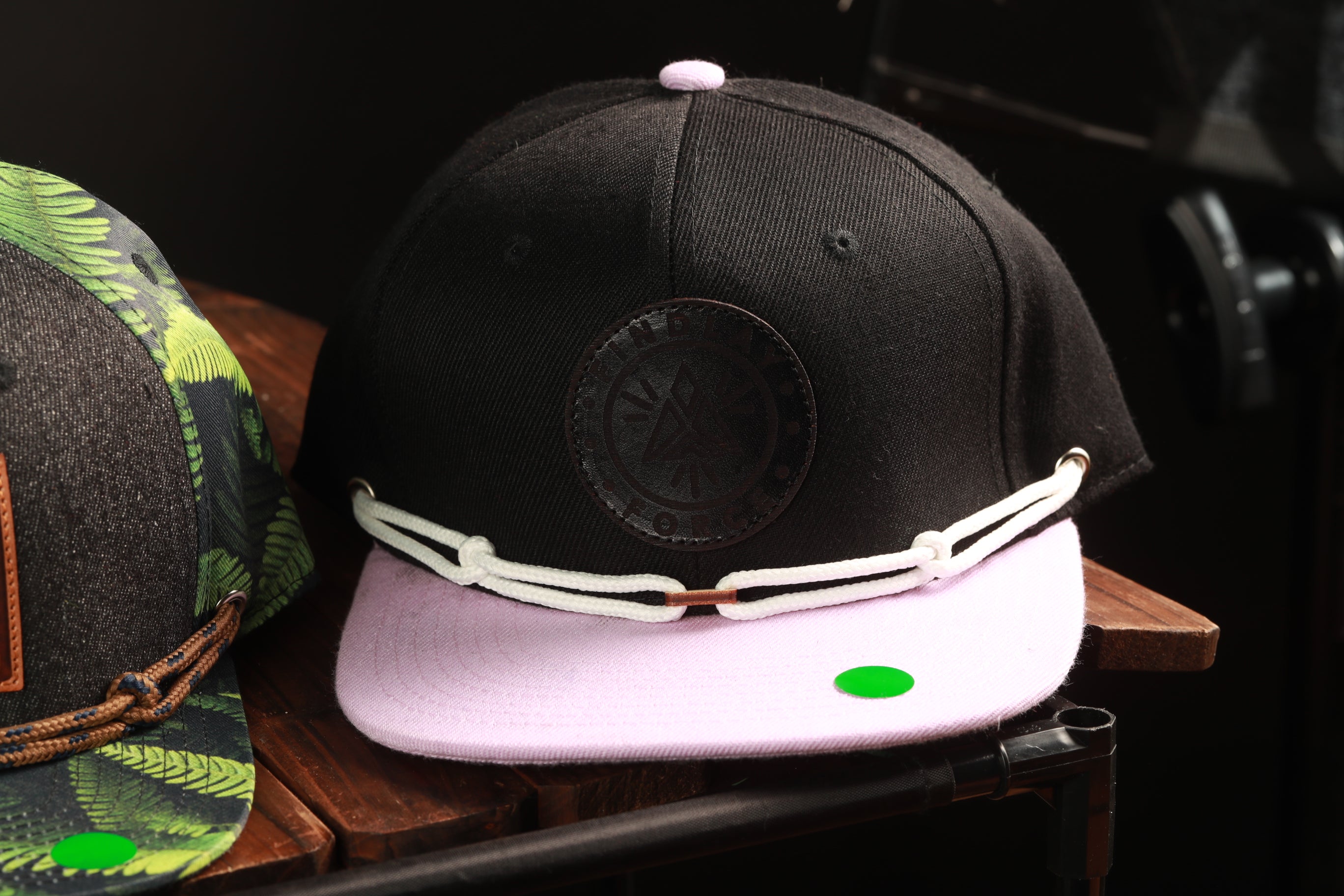 two baseball caps, one black and one pink, sitting on a wooden surface.