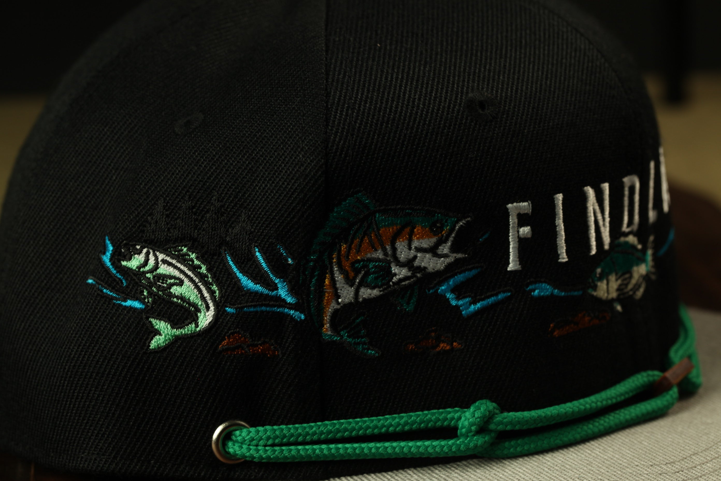A close-up view of a black baseball cap with colorful embroidered designs, including fish and other aquatic elements.