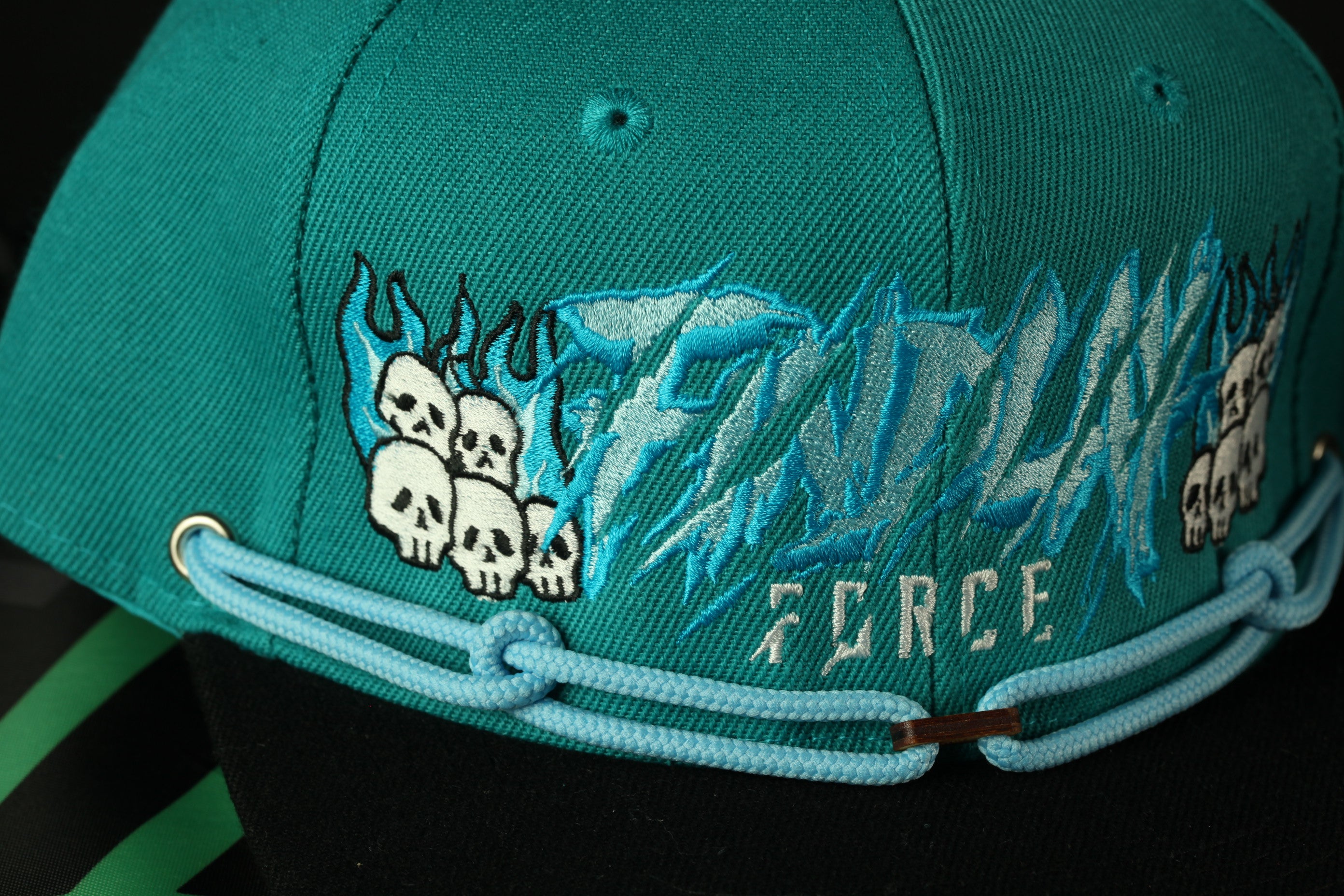 A close-up view of a turquoise baseball cap with a blue chain strap and a design featuring skull motifs.
