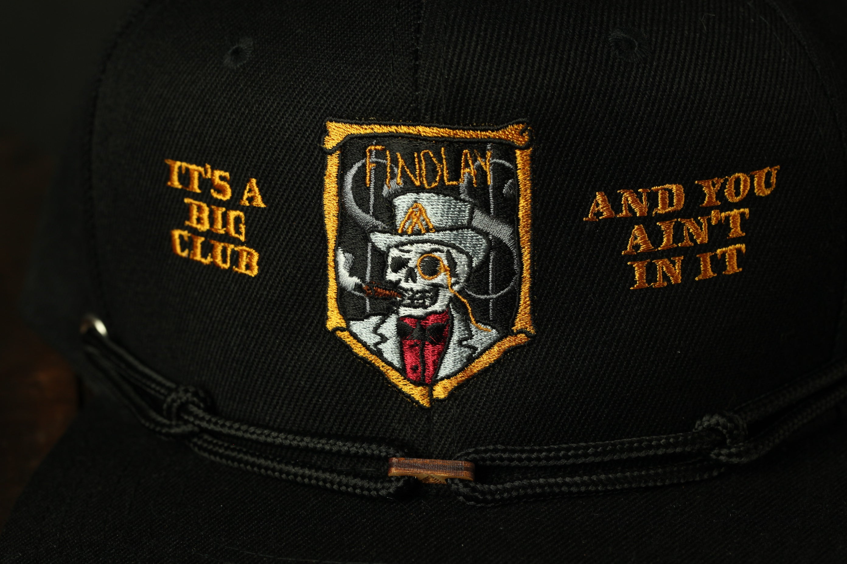 A close-up view of a black baseball cap with an embroidered logo on the front.
